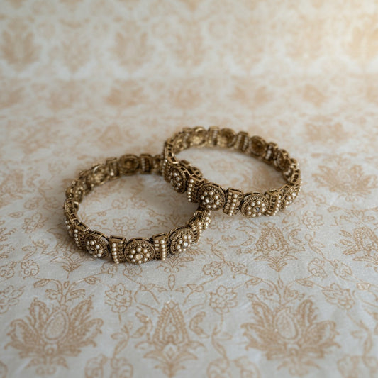 Two ornate gold bracelets on a textured beige surface