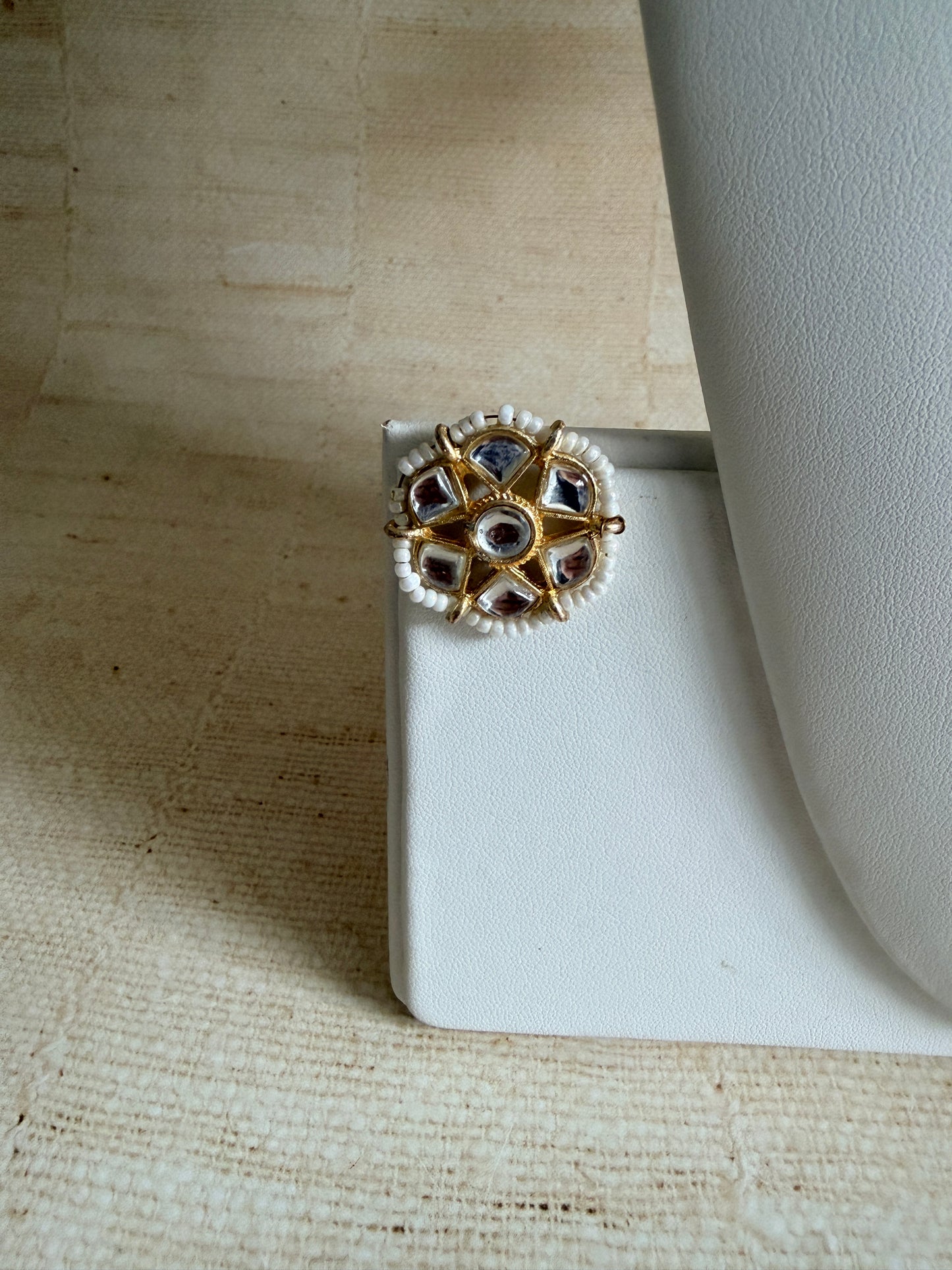 Gold and silver ring with gemstones on a white stand against a textured beige background