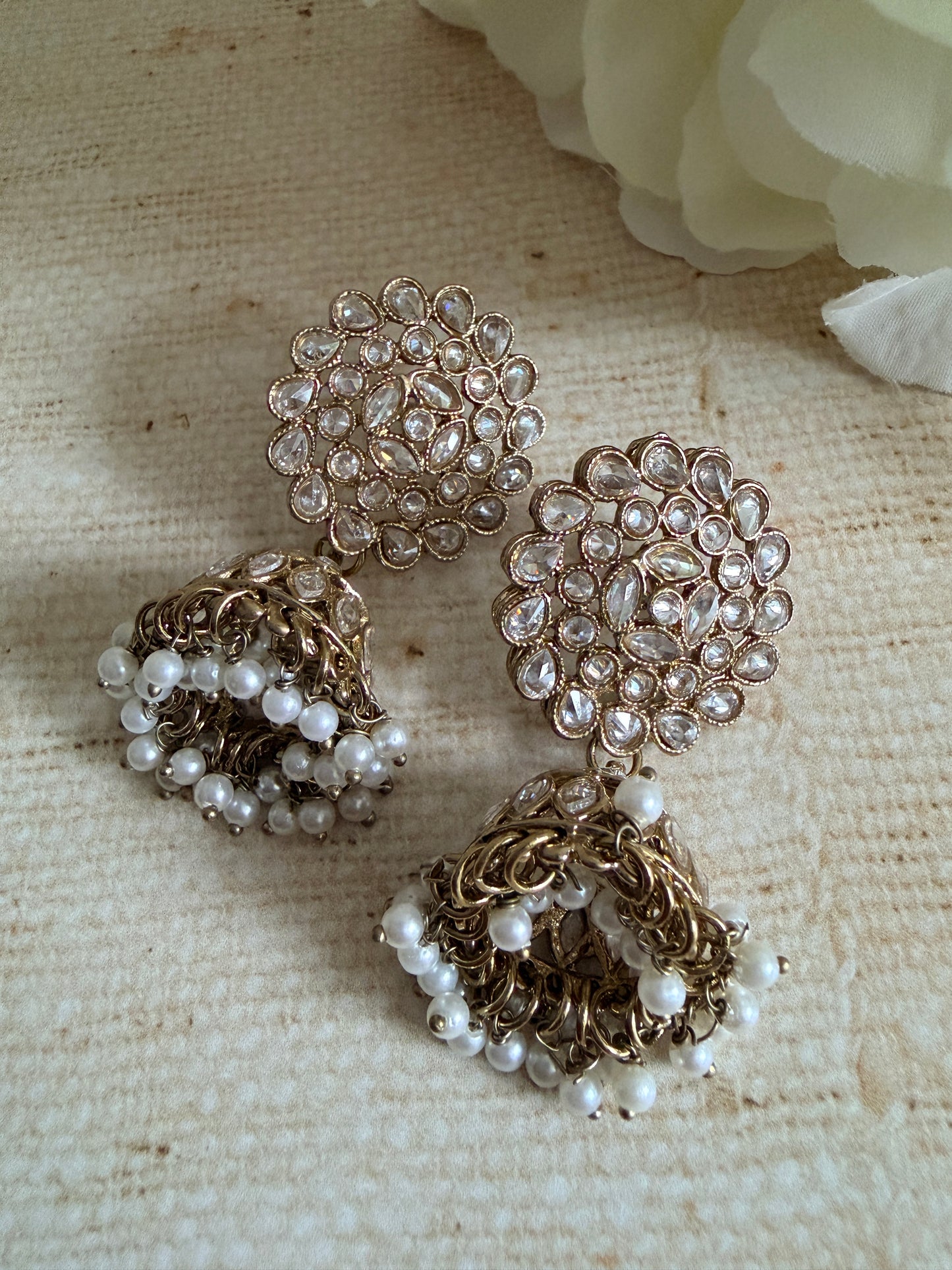 Pair of gold and pearl earrings on a textured beige surface with a white flower.