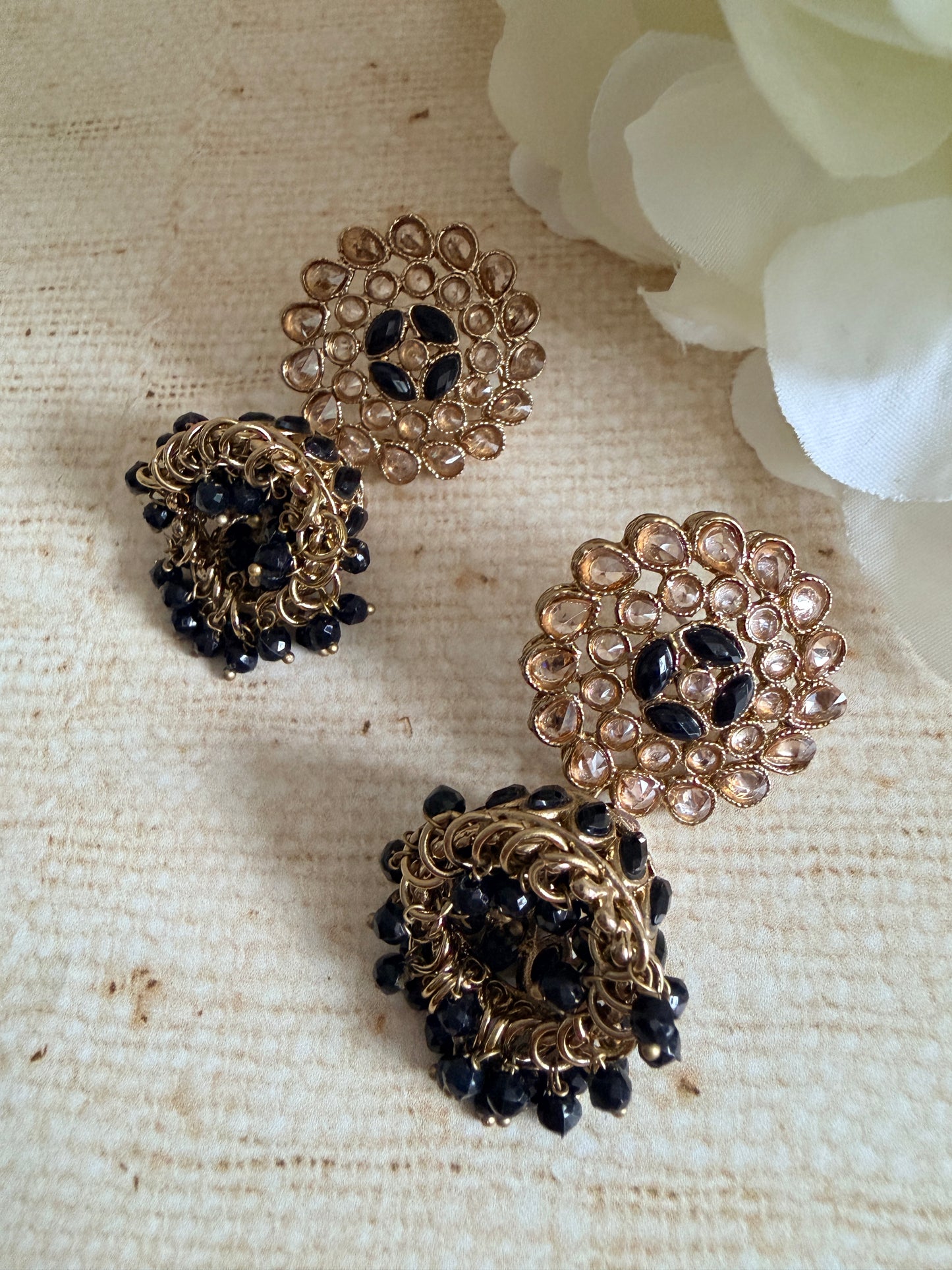 Gold and black beaded earrings on a textured beige surface with white flowers in the background.