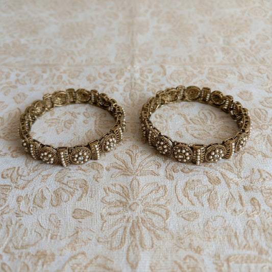Two ornate gold bangles on a textured beige fabric background