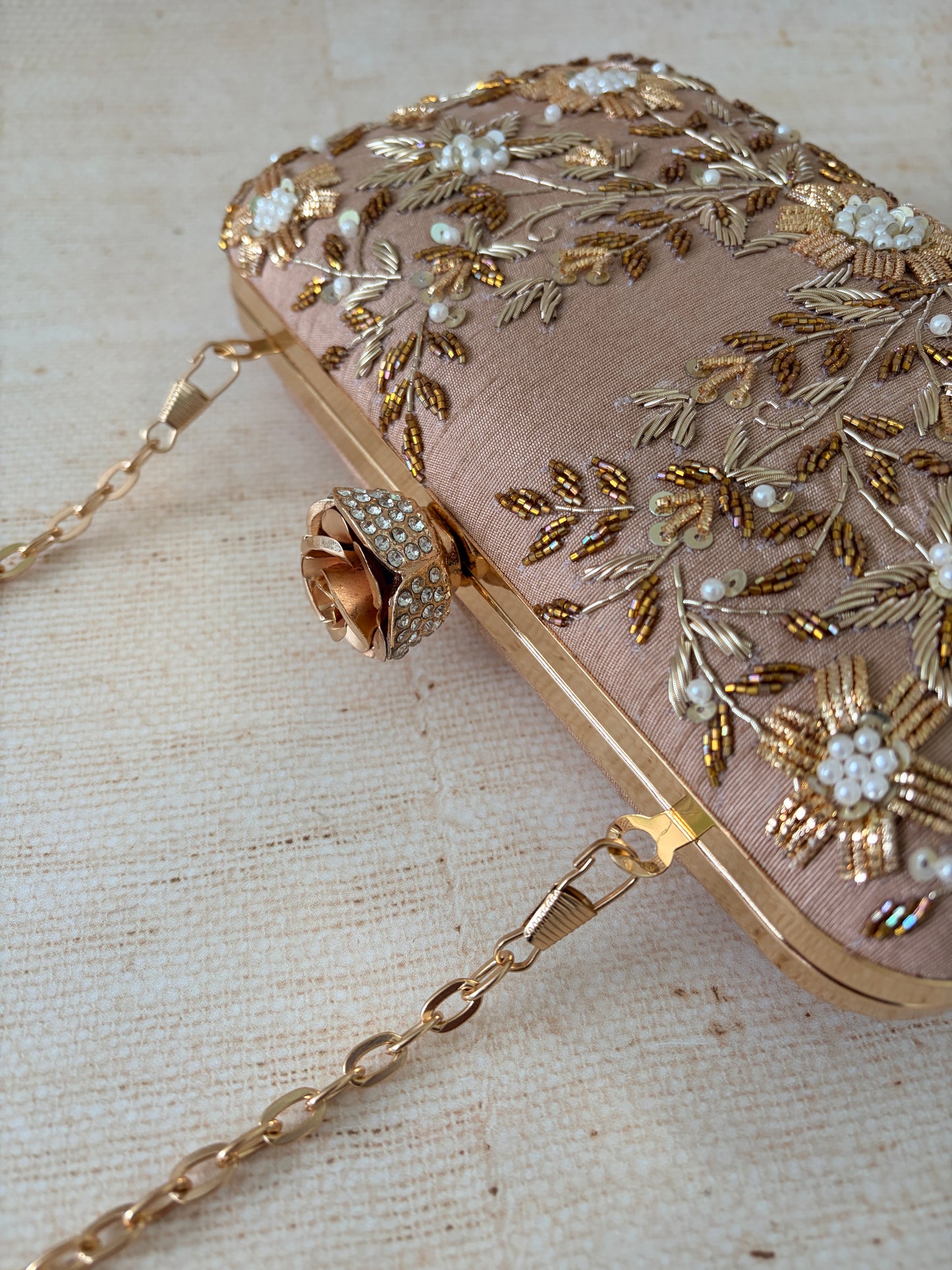 Pink handbag with gold embroidery and chain strap on a textured beige background