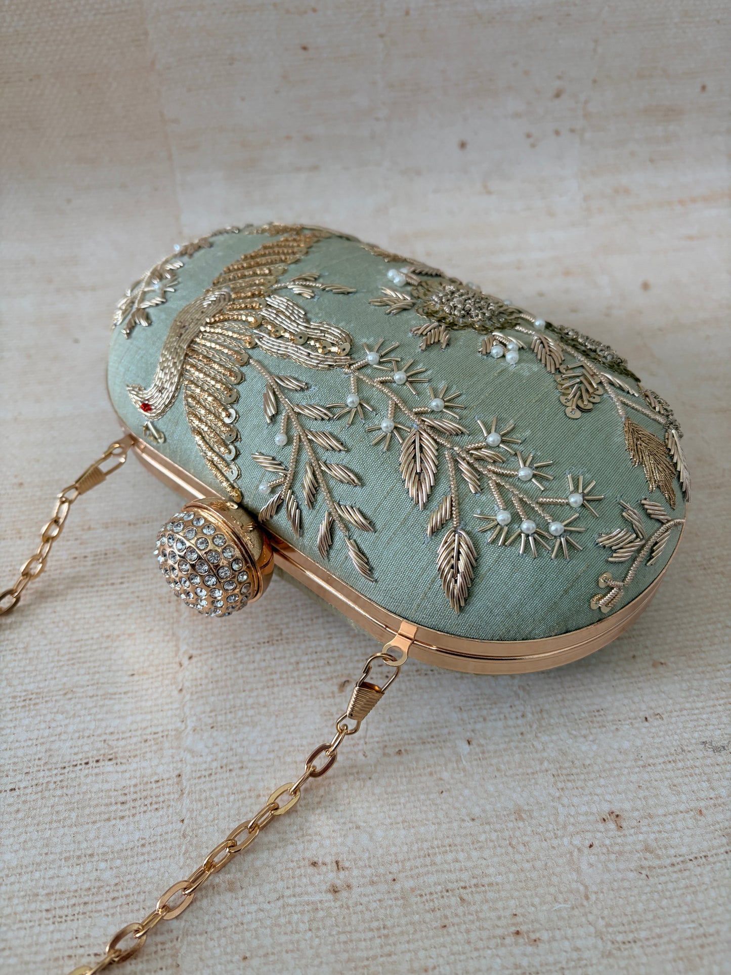 Decorative handbag with intricate gold embroidery on a textured beige background