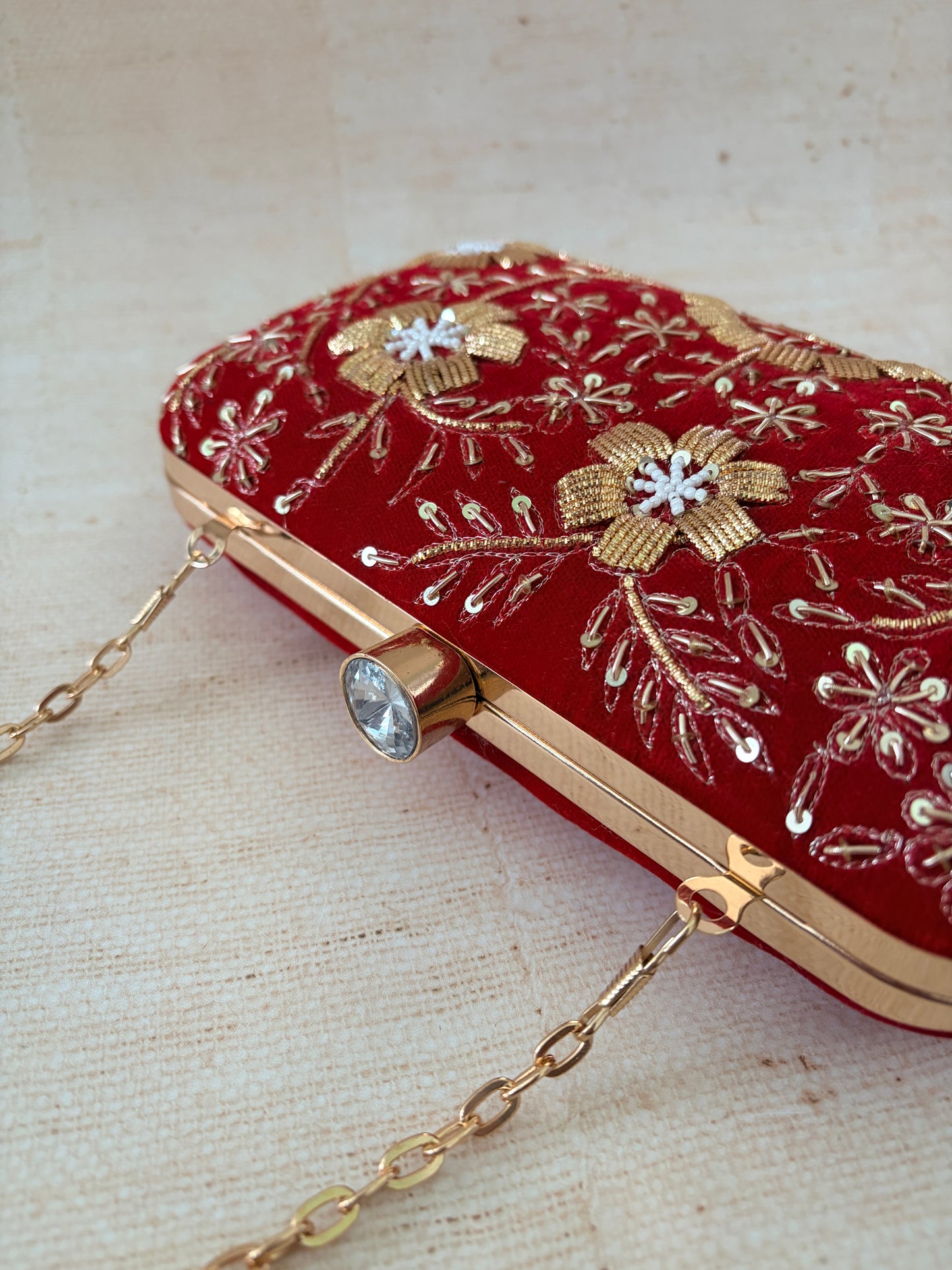 Red handbag with gold embroidery and chain strap on a beige background