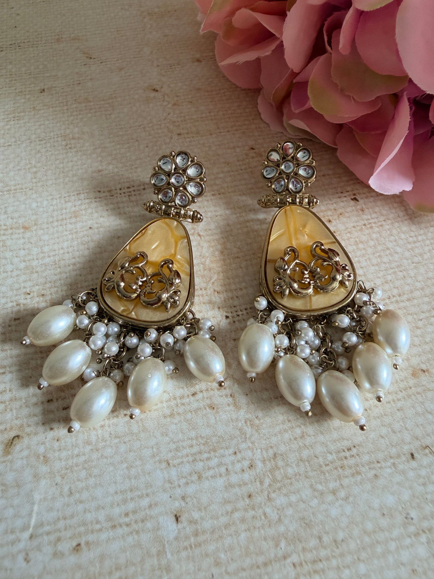 Pair of gold and pearl earrings on a textured surface with pink flowers.