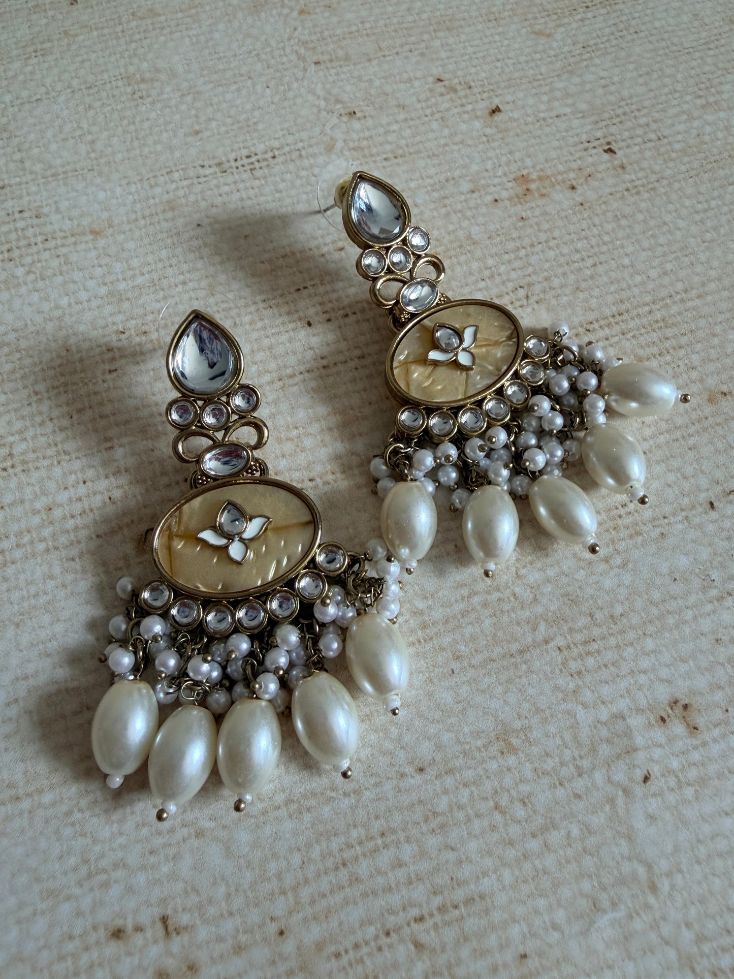 Pair of ornate earrings with pearls on a textured surface