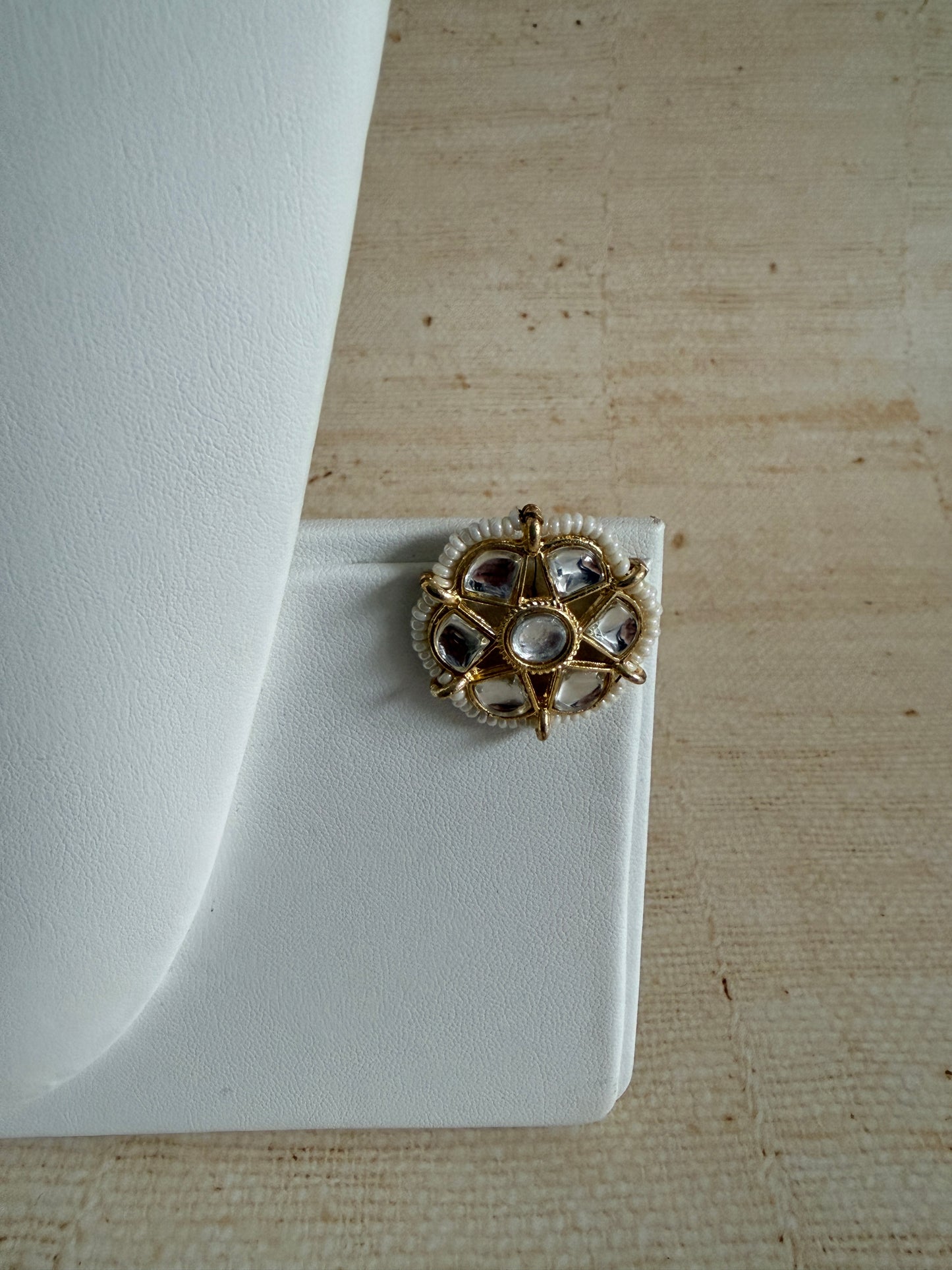 Gold and crystal earring on a white cushion against a beige textured background