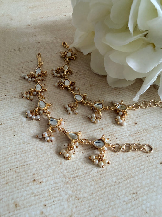 Gold necklace with pearl-like stones on a textured surface with white flowers.