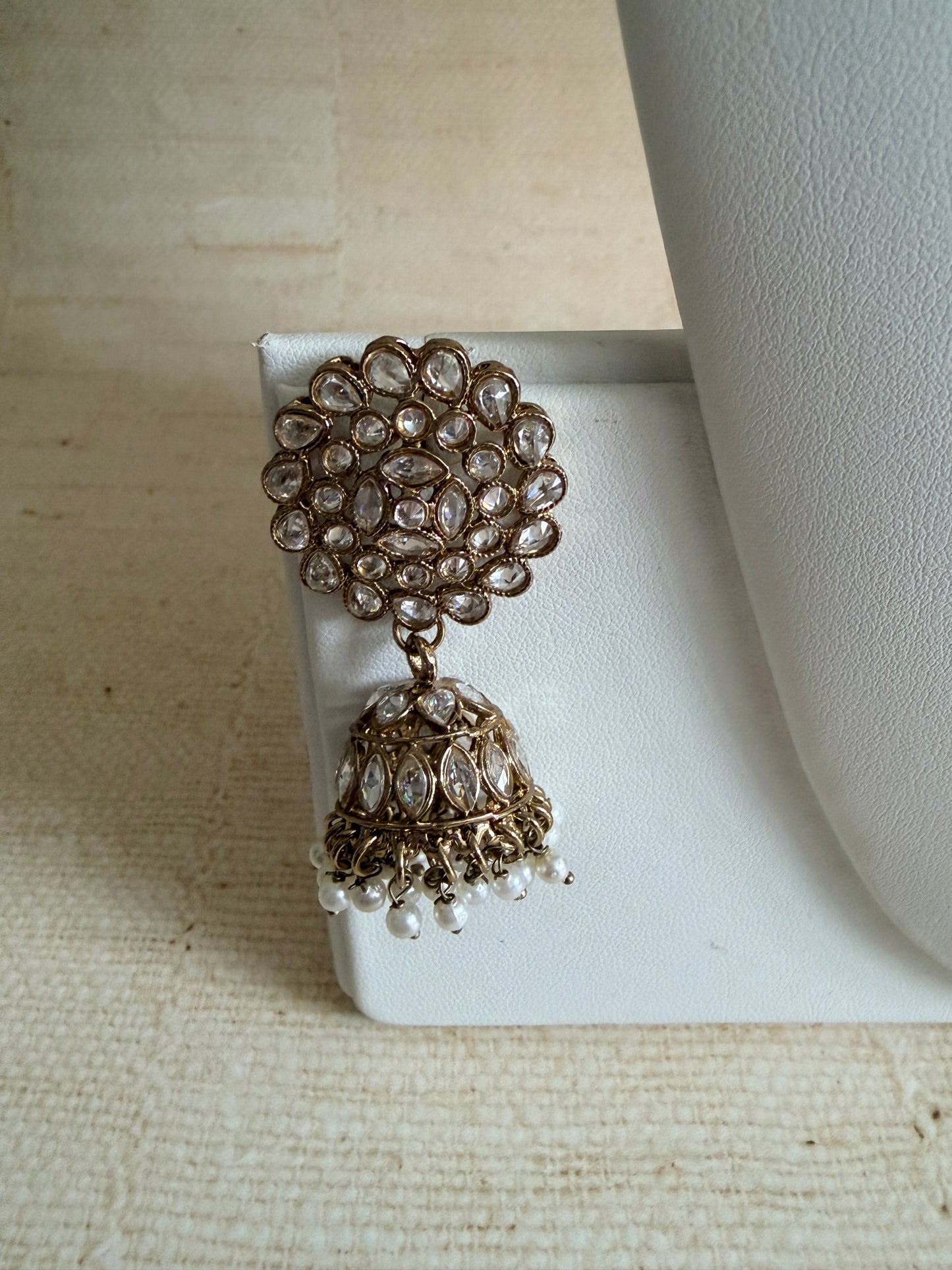 Pair of ornate earrings on a white stand with a textured beige background