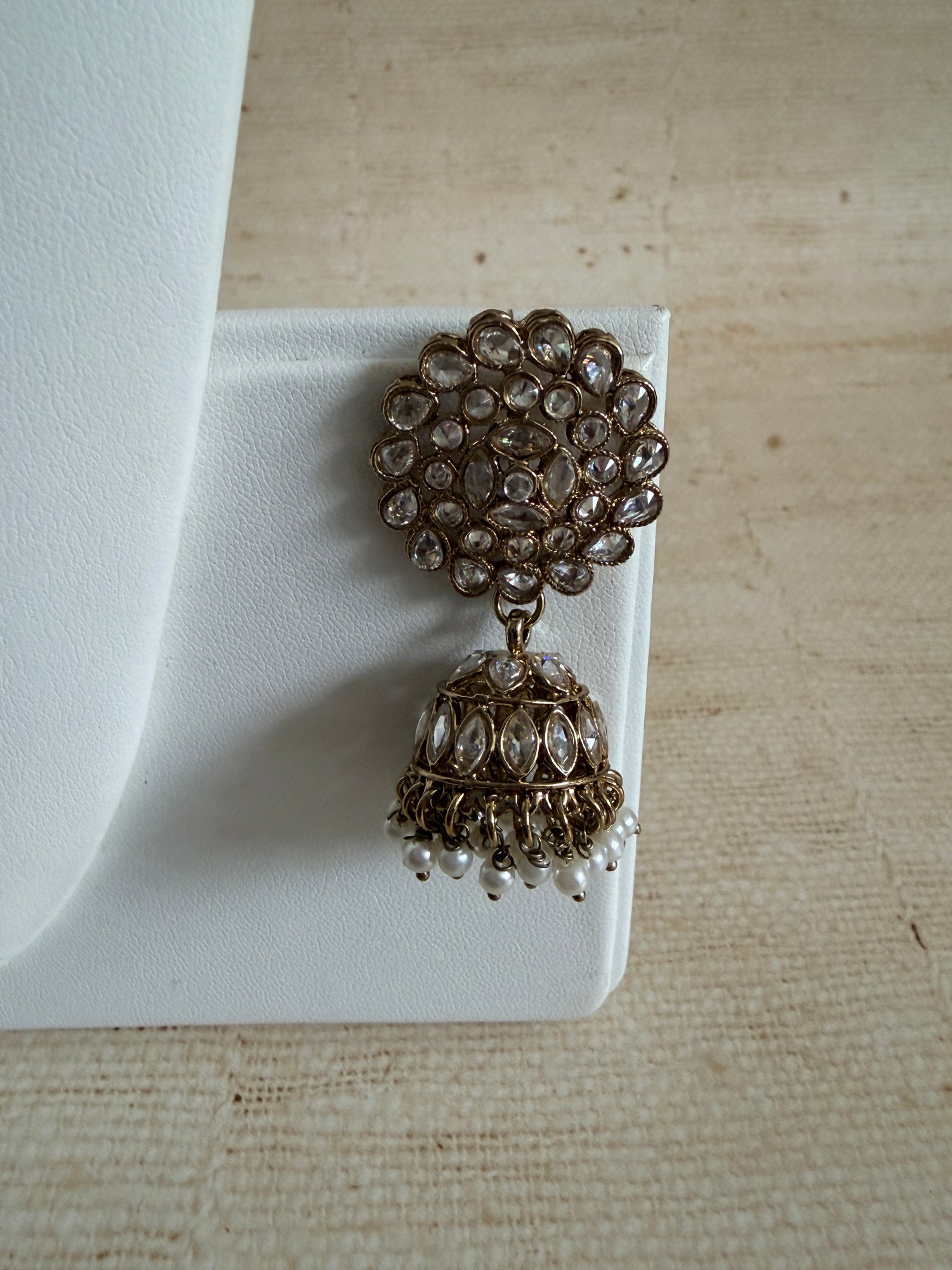 Pair of ornate earrings on a white stand against a beige background