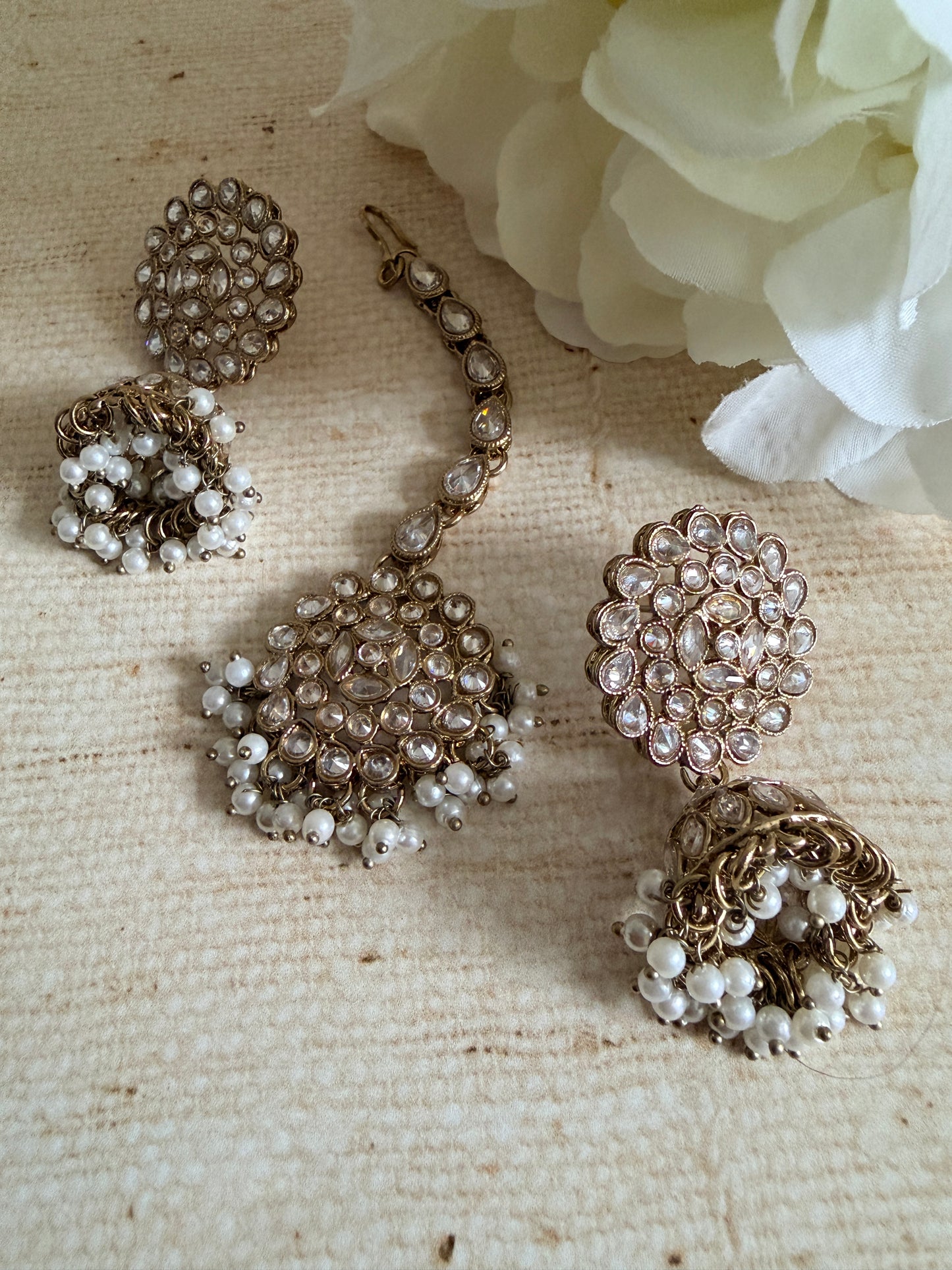 Set of pearl and crystal jewelry on a textured beige surface with a white flower.