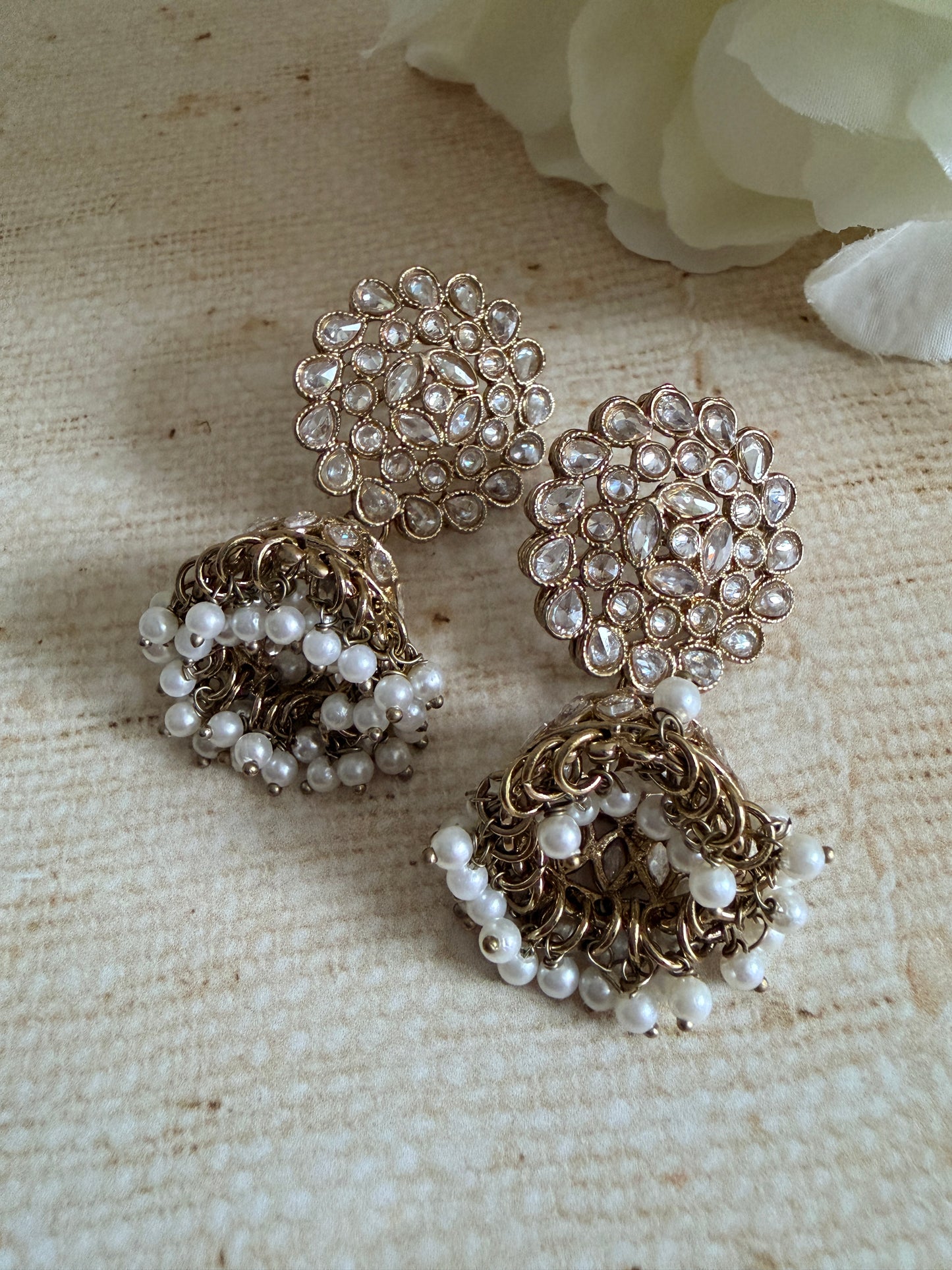 Gold and pearl jewelry pieces on a textured beige surface with a white flower.