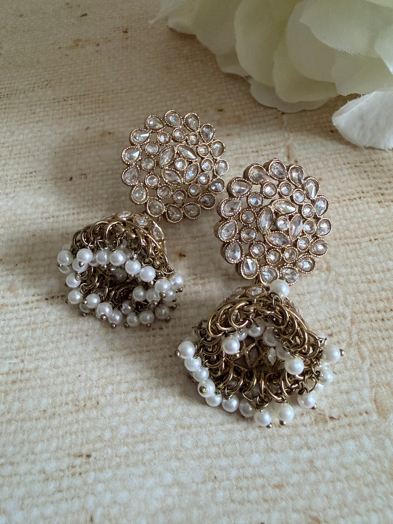 Gold and pearl jewelry pieces on a textured beige surface with a white flower.
