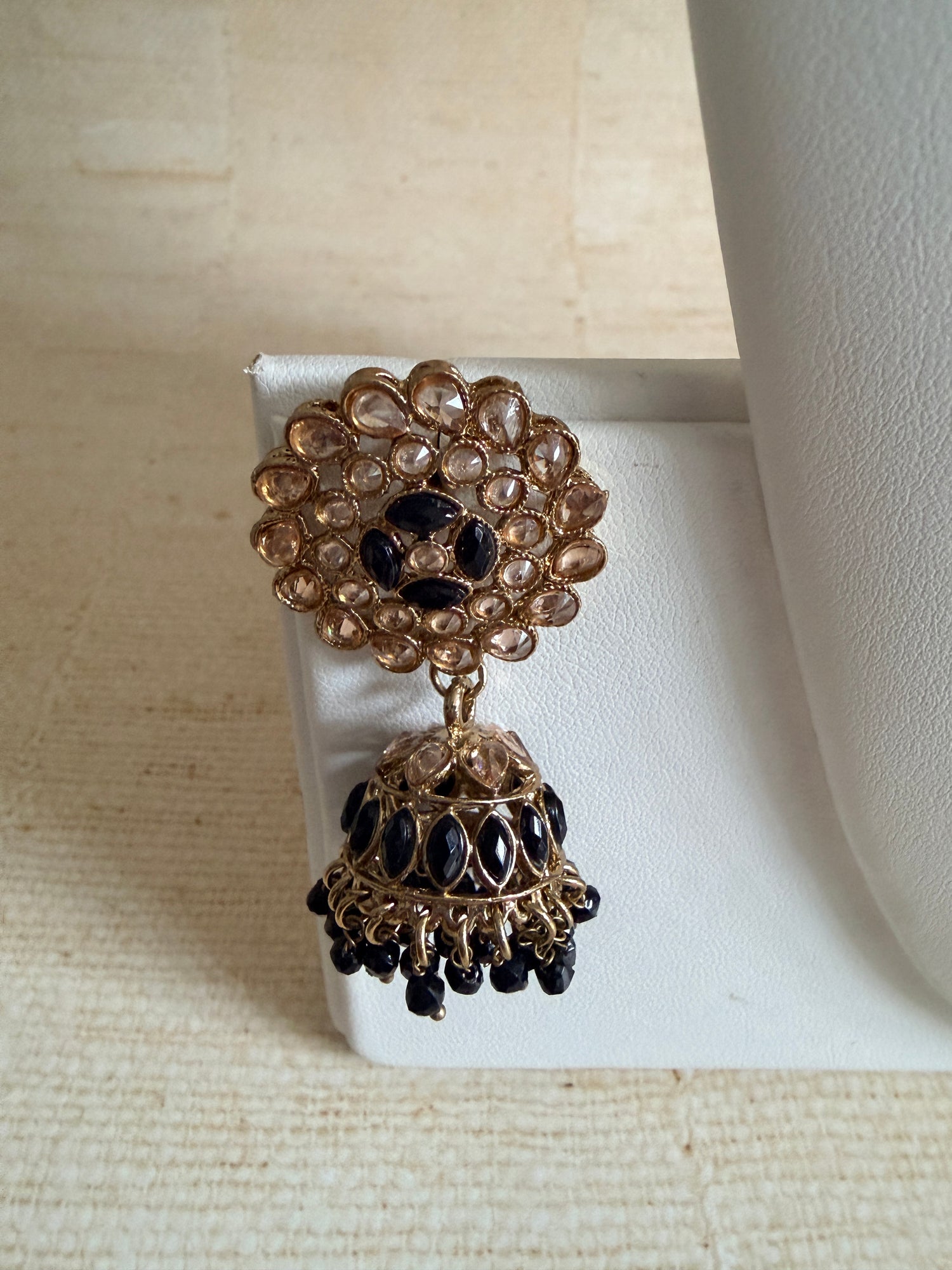 Gold and black earrings on a white stand with a beige background