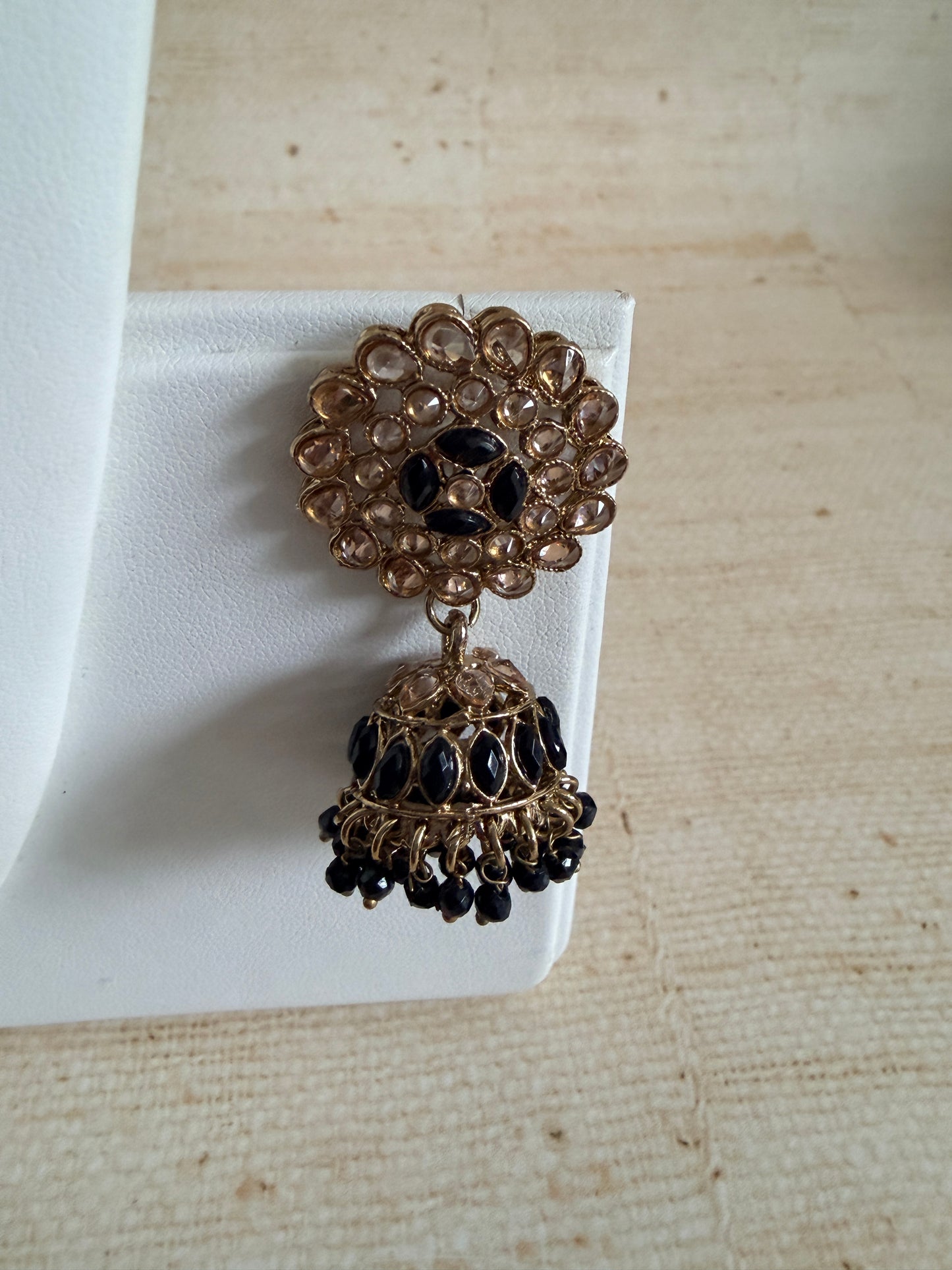 Pair of gold and black earrings on a white cloth with a beige fabric background