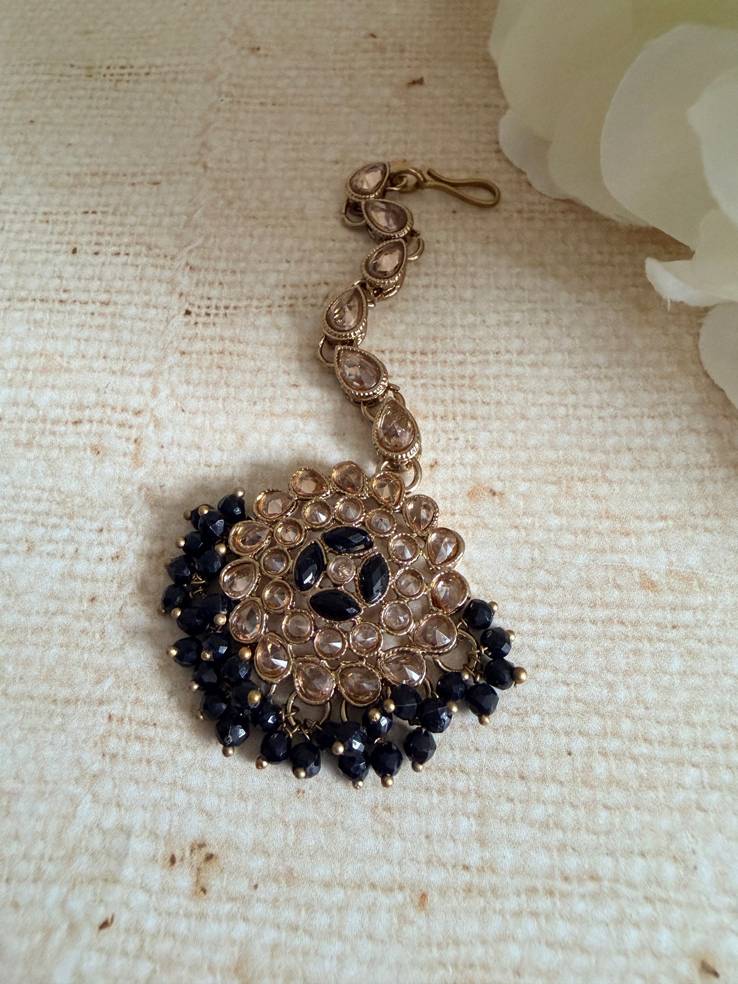 Decorative hair clip with black and gold beads on a textured beige background