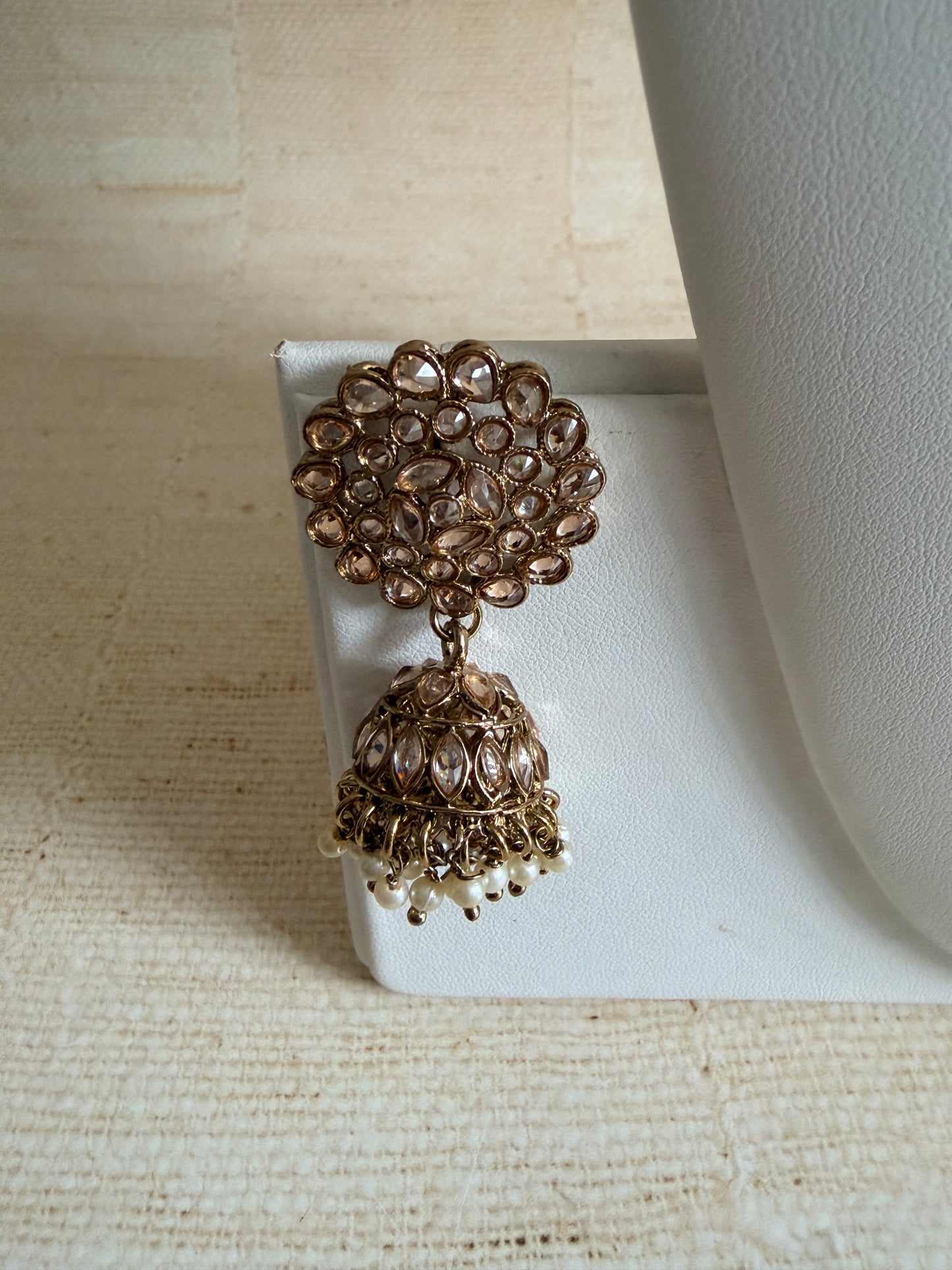 Gold earrings on a white stand against a beige background