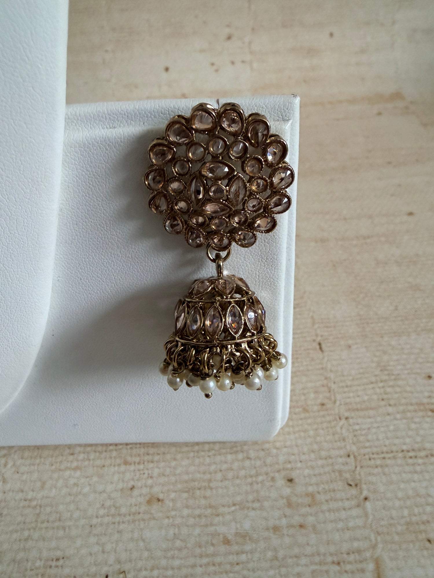 Pair of gold and pearl earrings on a white stand with a beige textured background