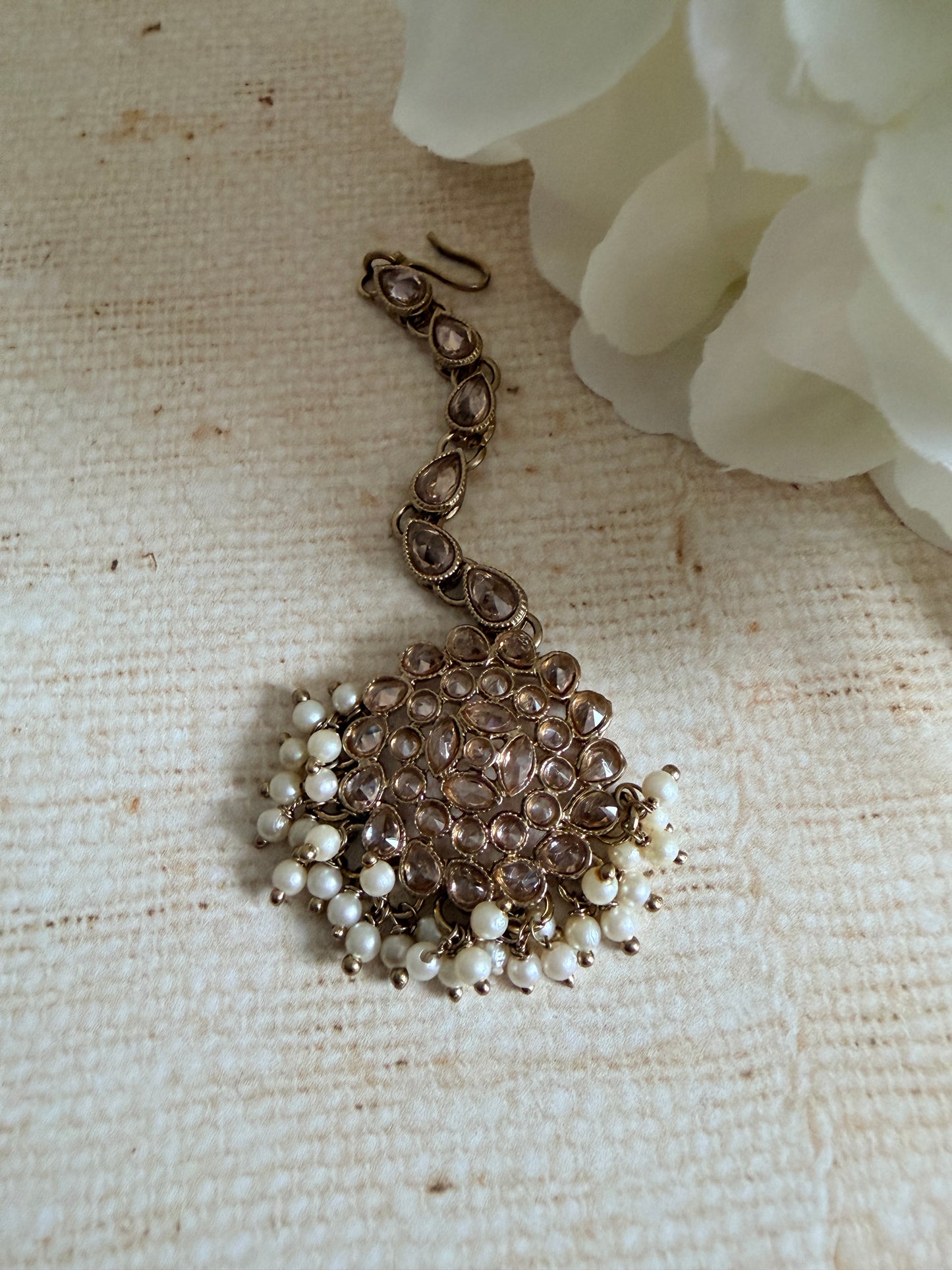 Pearl and bronze necklace on a textured beige surface with white flowers.