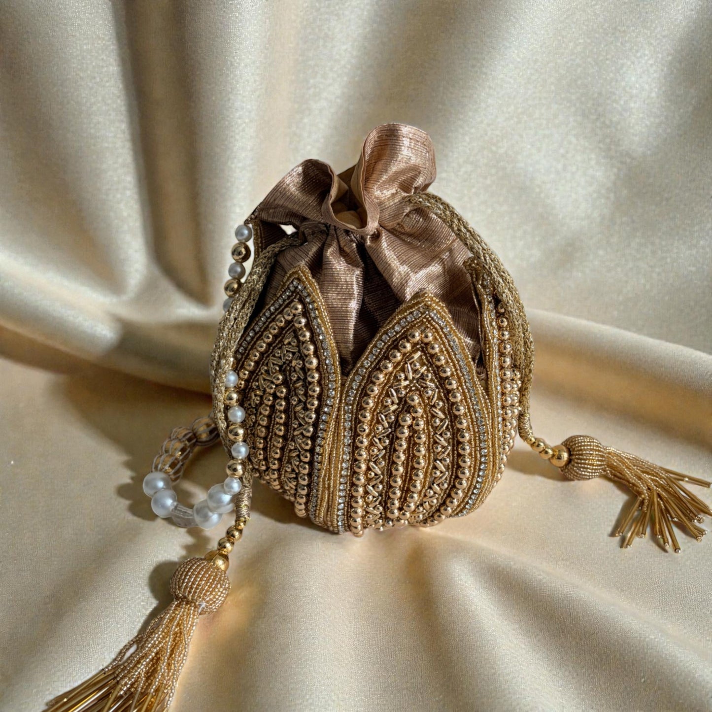 Decorative handbag with intricate gold embroidery and tassels on a beige fabric background