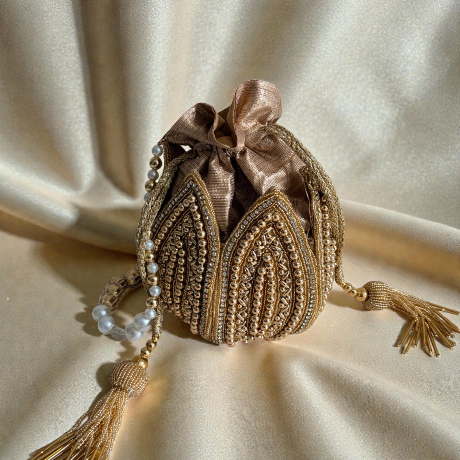 Decorative handbag with intricate gold embroidery and tassels on a beige fabric background