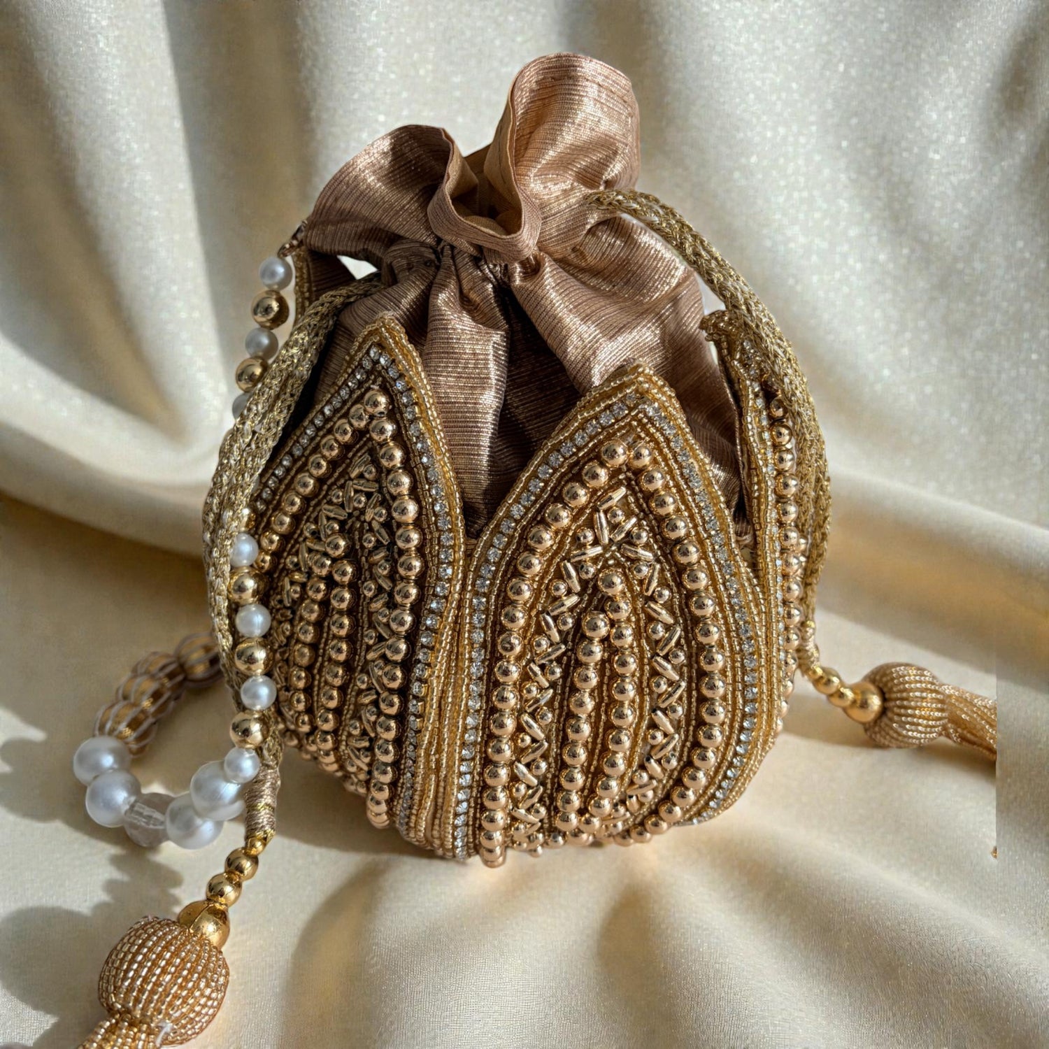 Decorative handbag with gold embroidery and pearl details on a beige fabric background
