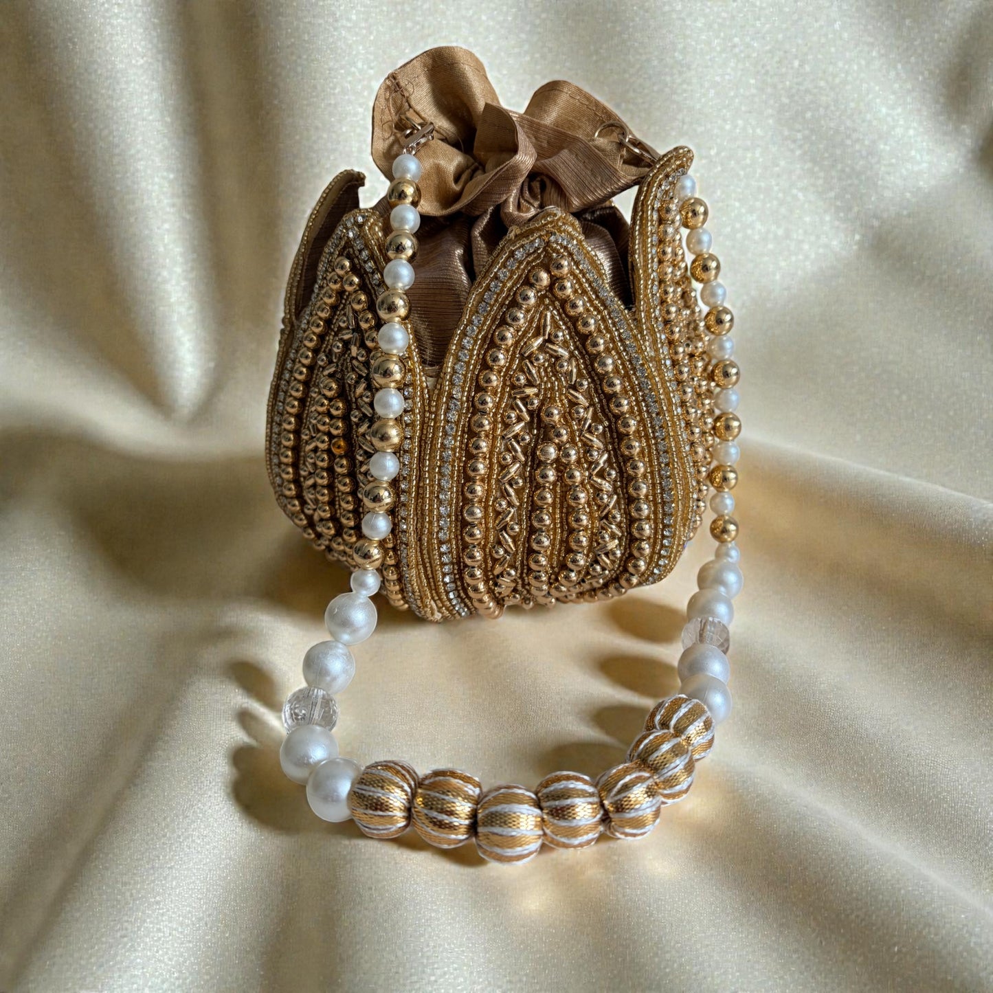 Decorative gold purse with pearl embellishments on a beige fabric background