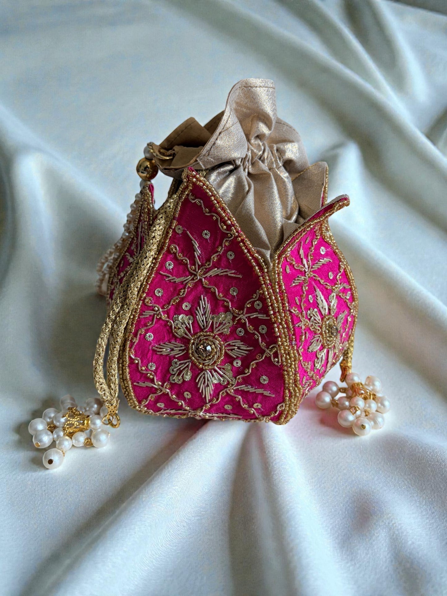 Decorative pink handbag with gold embroidery on a white fabric background