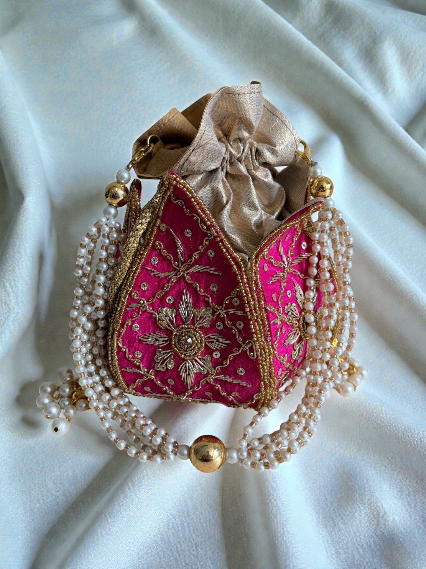 Decorative handbag with pink fabric, gold embroidery, and pearl detailing on a white fabric background