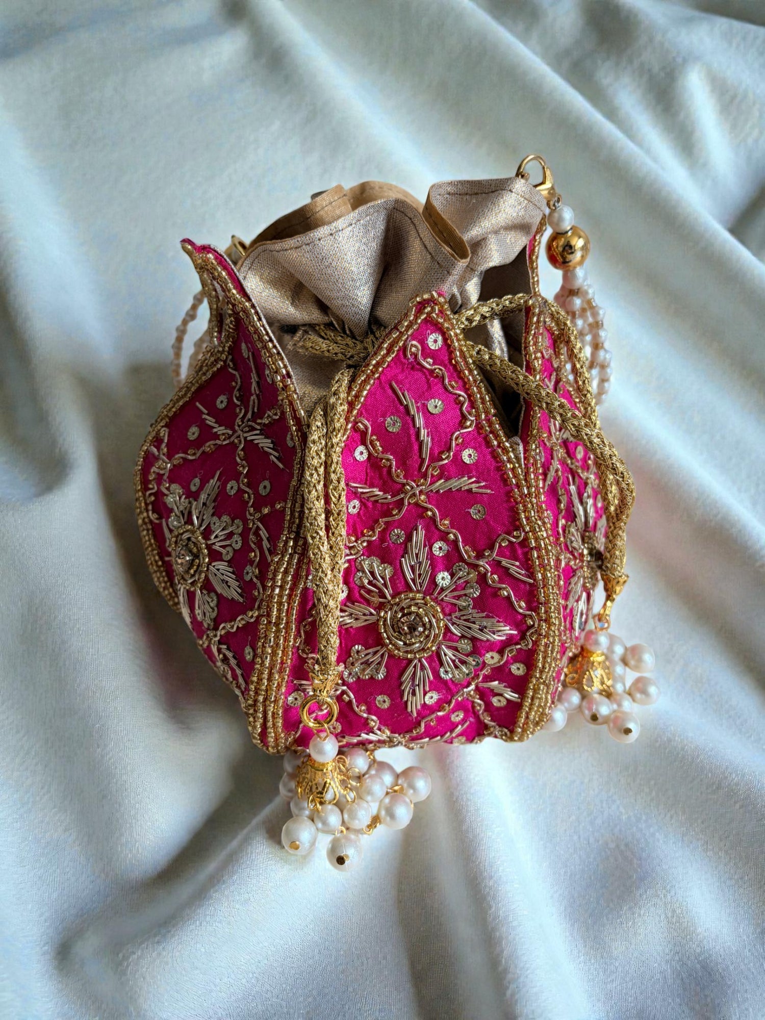 Decorative pink fabric pouch with gold embroidery and pearl embellishments on a white fabric background
