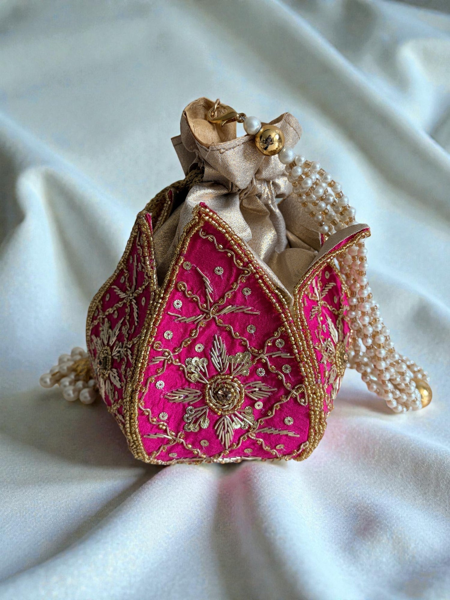 Decorative pink bag with gold embroidery on a white fabric background