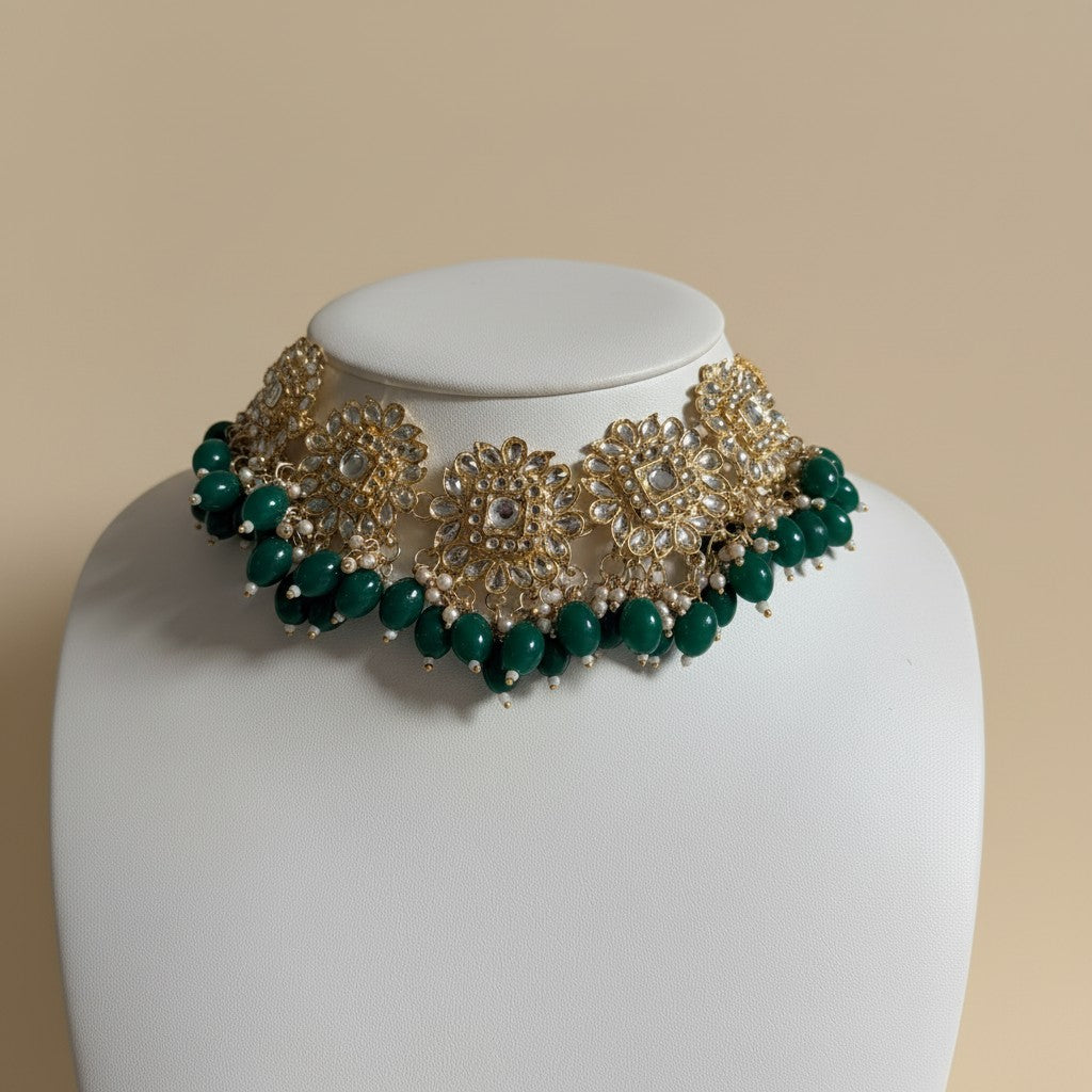 Green and gold necklace on a mannequin head against a beige background