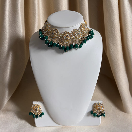 Green and gold necklace and earrings on a white mannequin bust against a beige curtain.