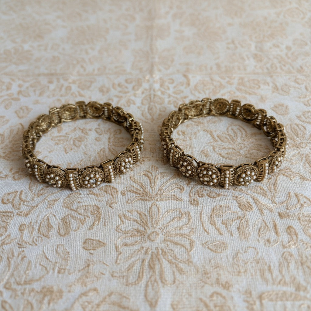 Two ornate gold bangles on a textured beige fabric background