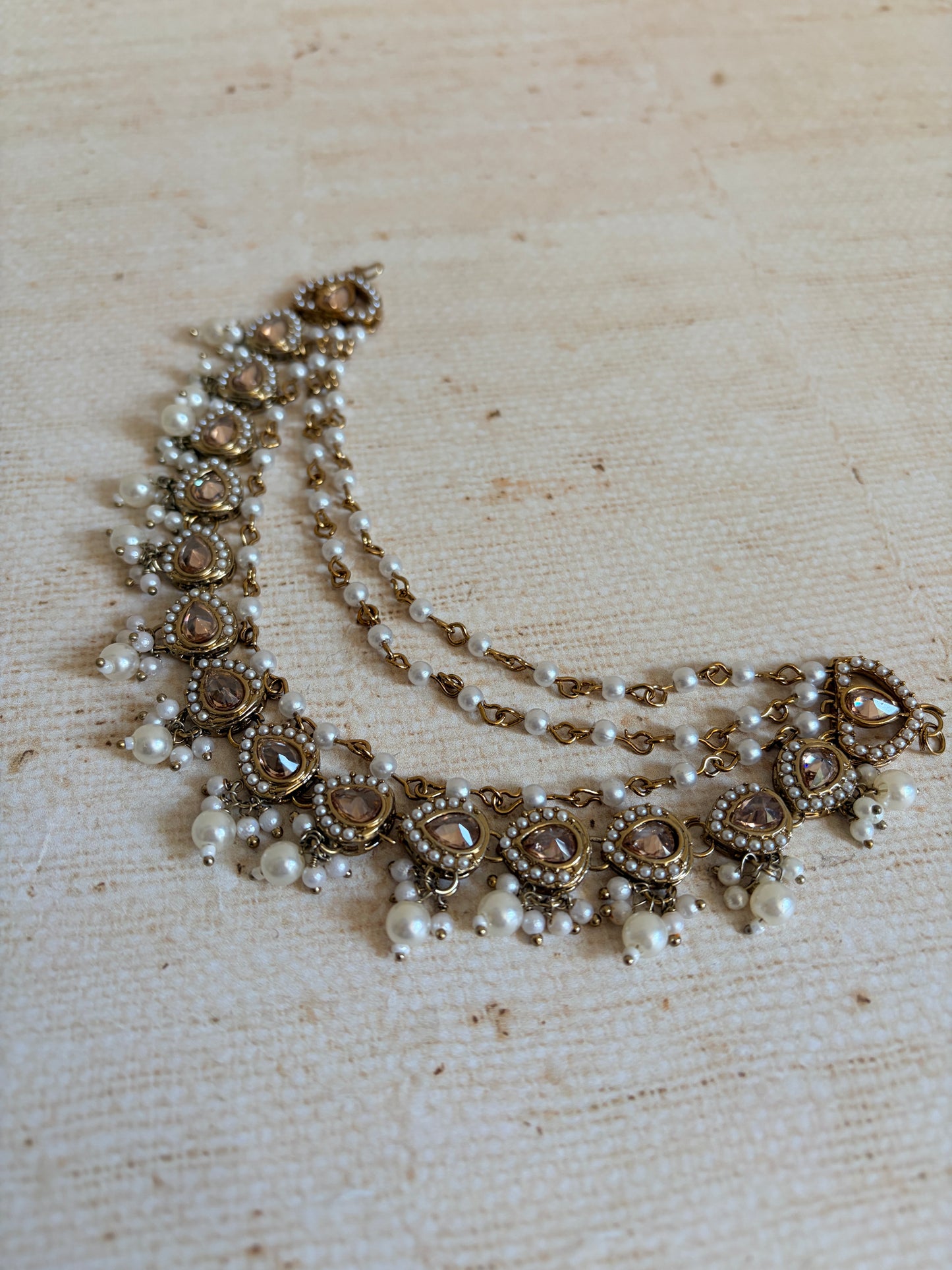 Decorative necklace with pearls and gold accents on a textured beige background