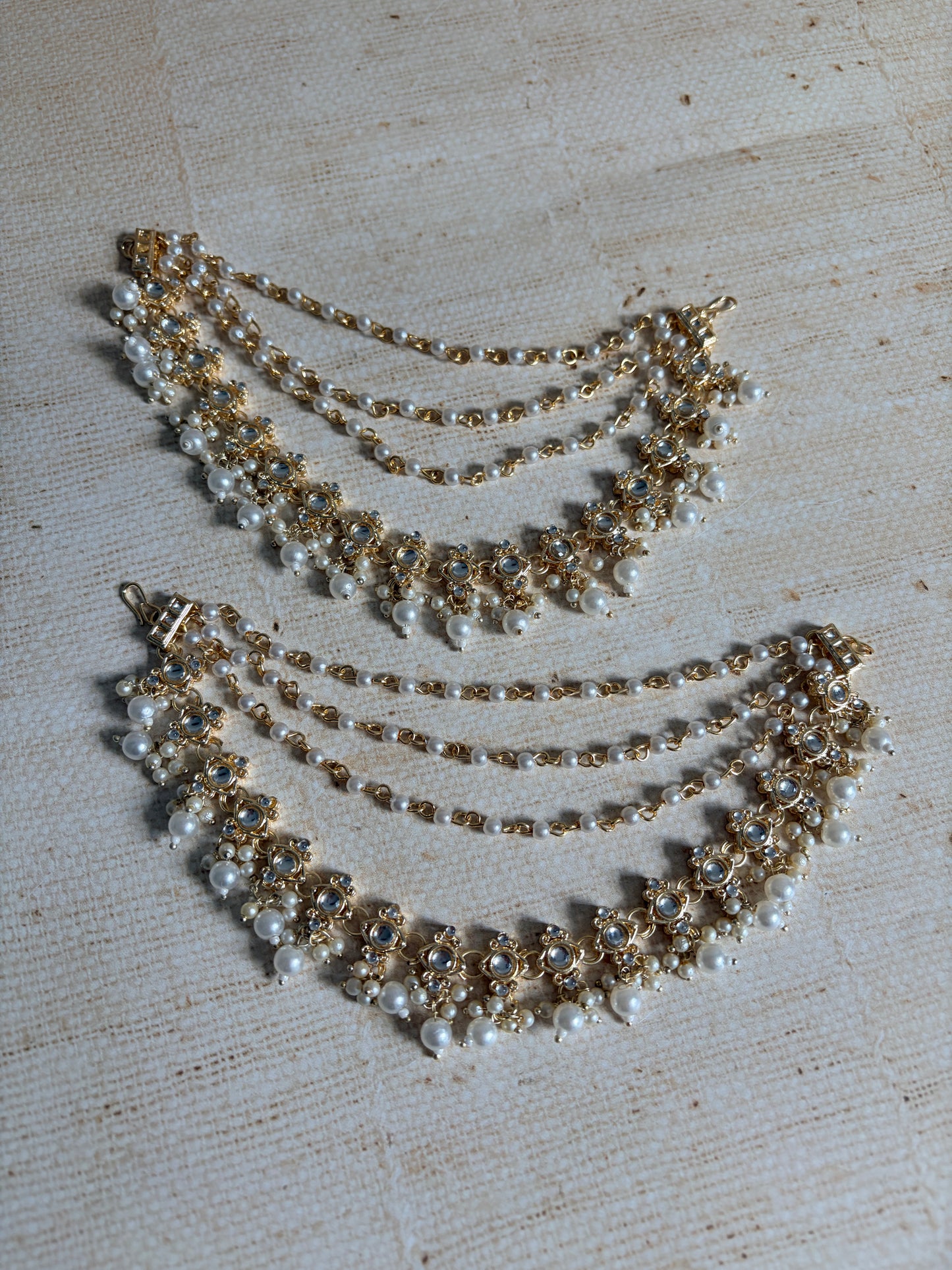Two pearl and gold necklaces on a textured beige surface