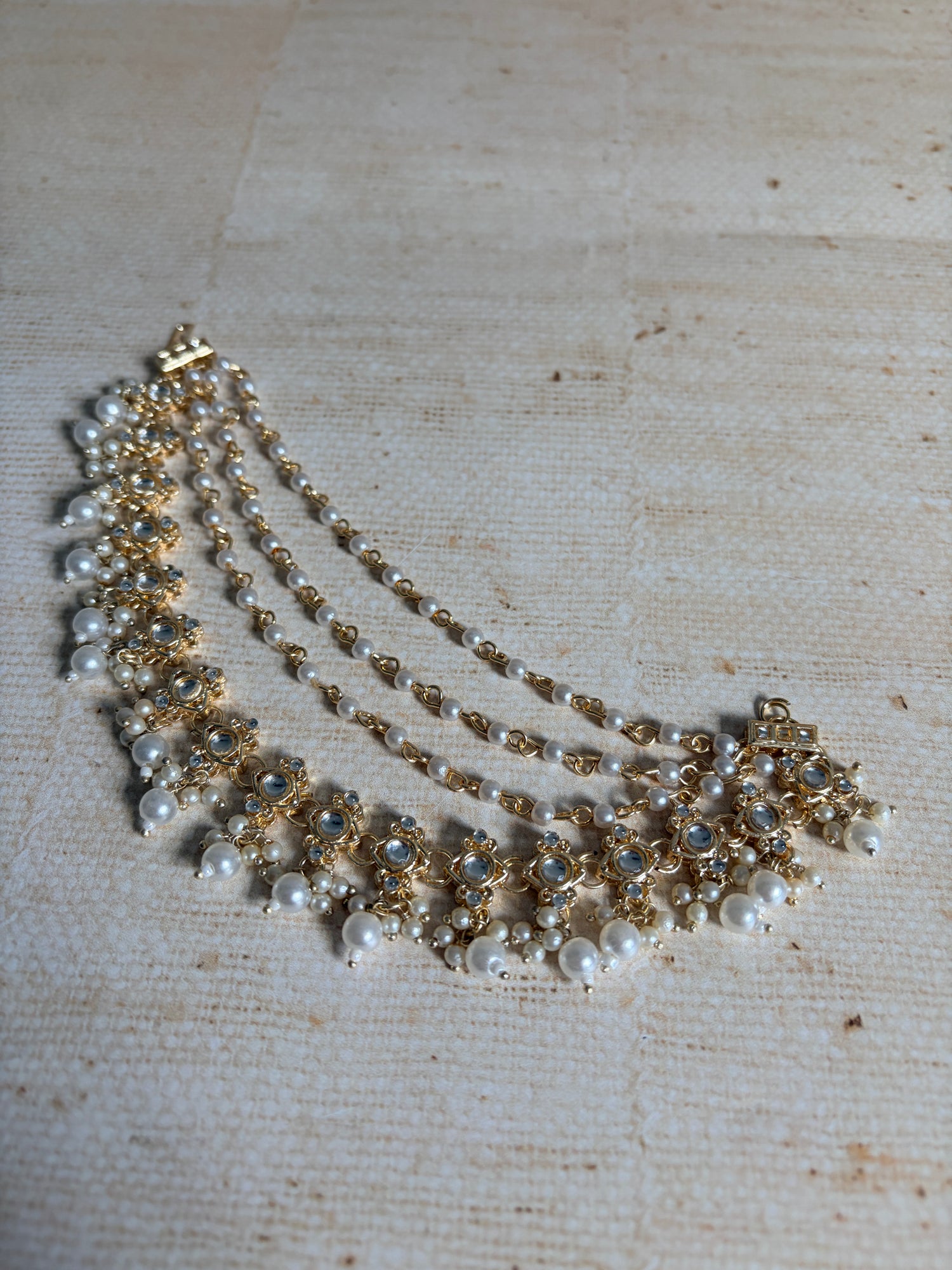 Delicate pearl and gold necklace on a textured beige background
