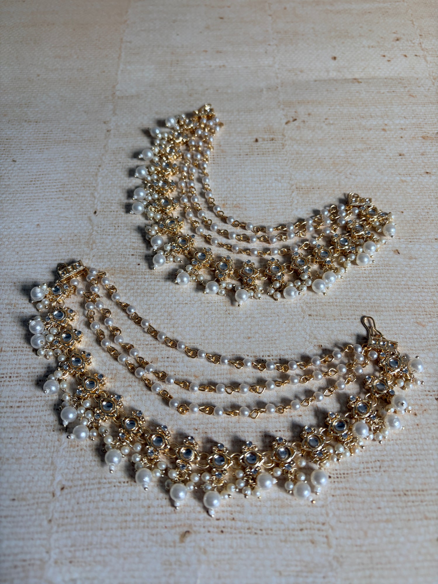 Two pearl and gold necklaces on a textured beige surface