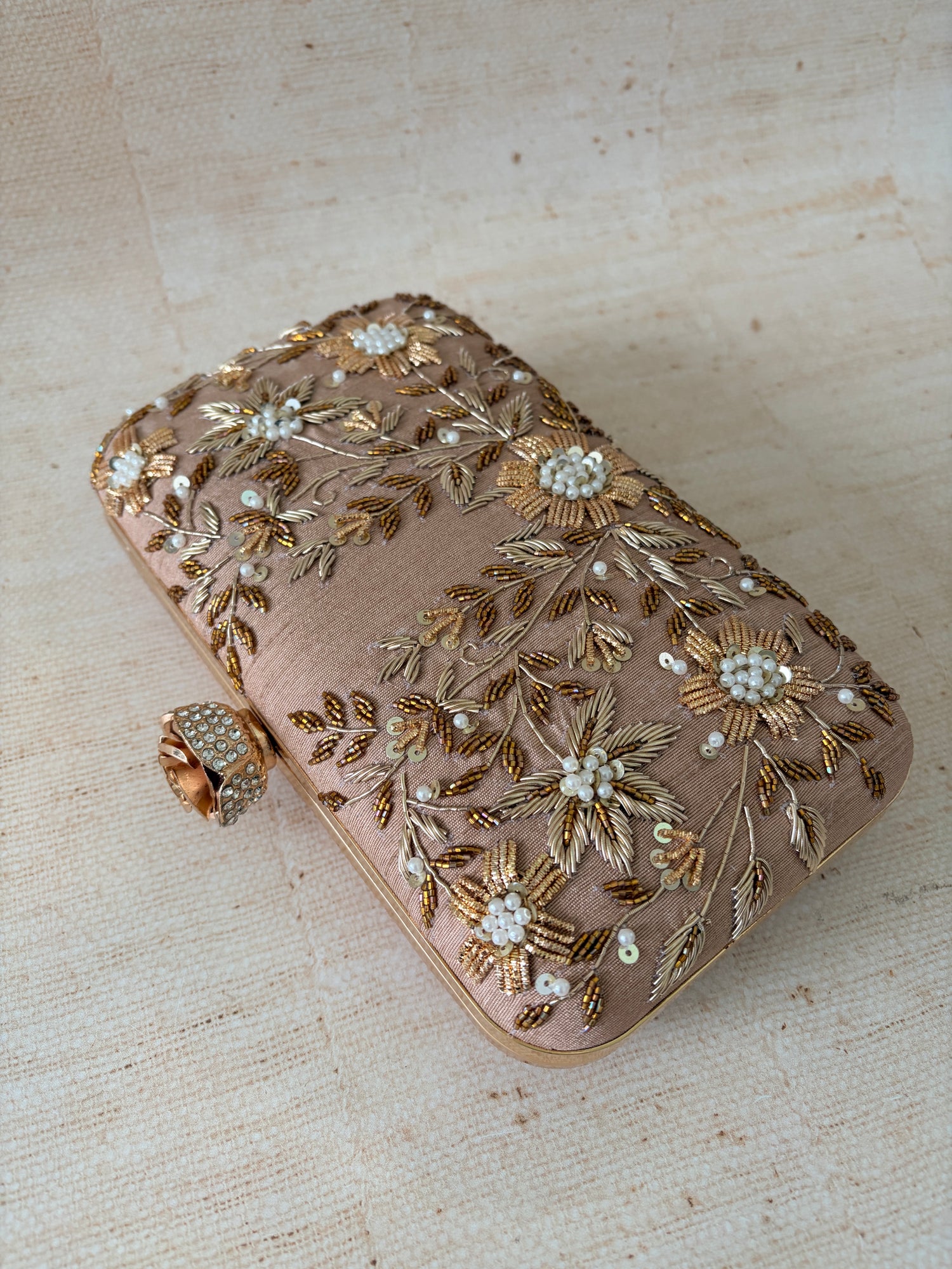 Decorative clutch bag with floral embroidery on a textured beige surface