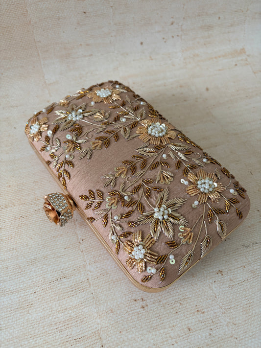 Decorative clutch bag with floral embroidery on a textured beige surface