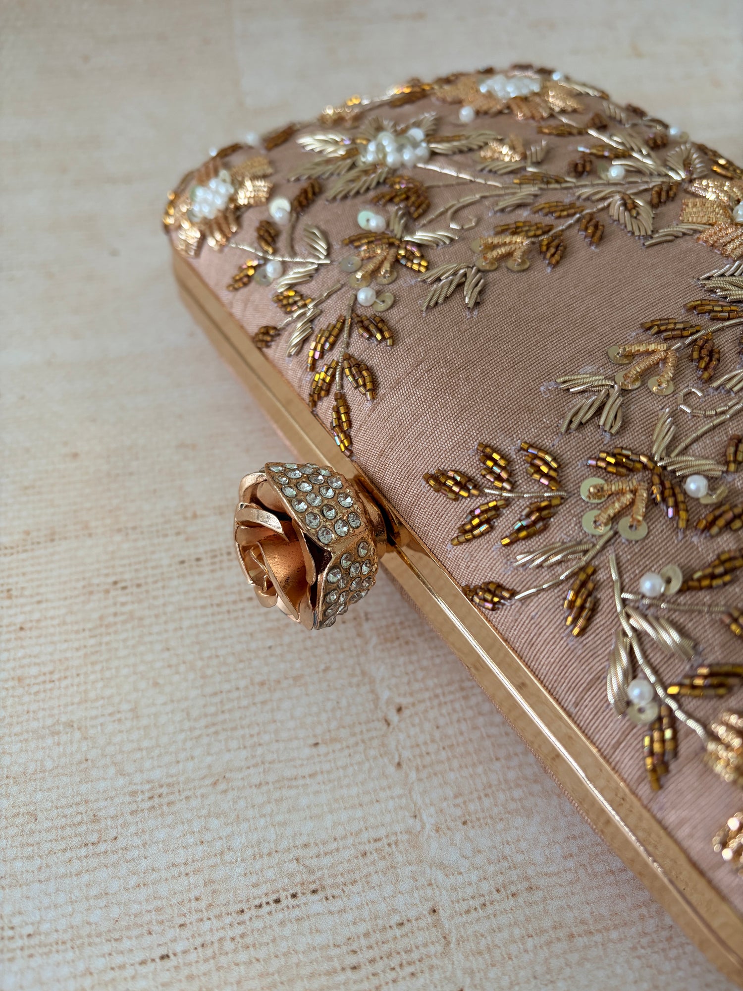 Decorative clutch with gold embroidery and a rose detail on a beige fabric background