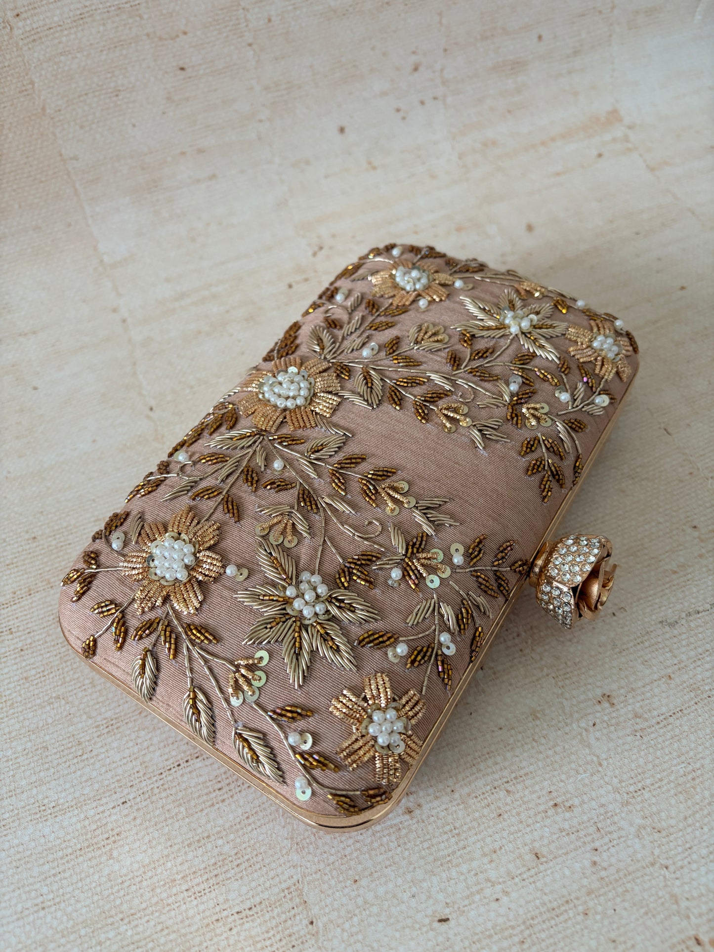 Decorative clutch bag with floral embroidery on a textured surface