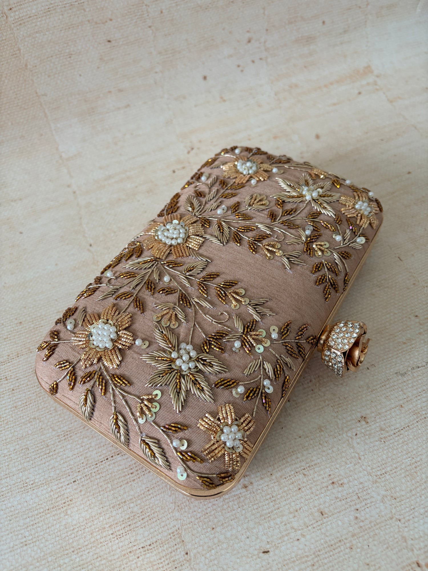 Decorative clutch bag with floral embroidery on a textured surface