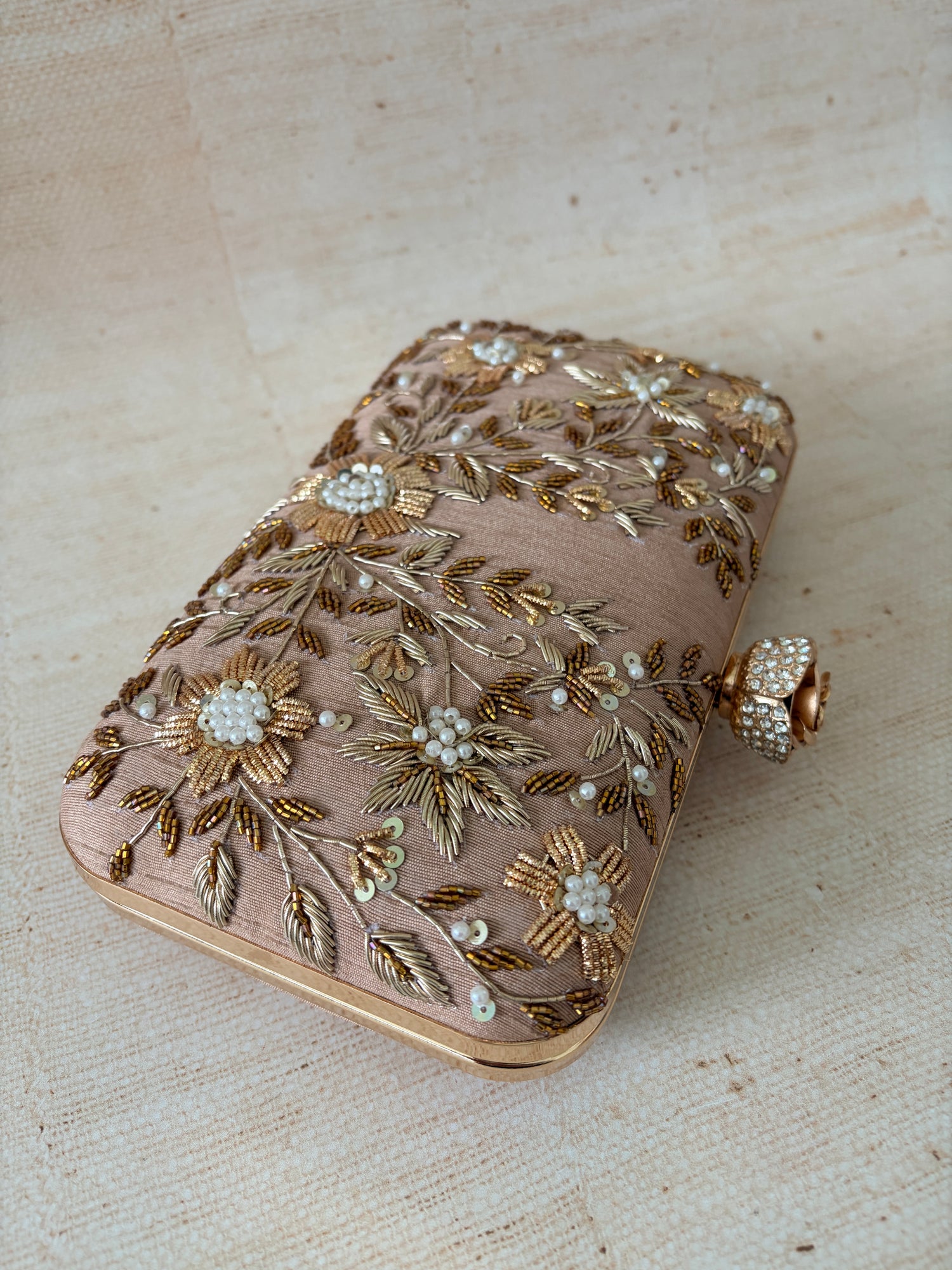 Decorative clutch with floral embroidery and pearl embellishments on a textured beige background