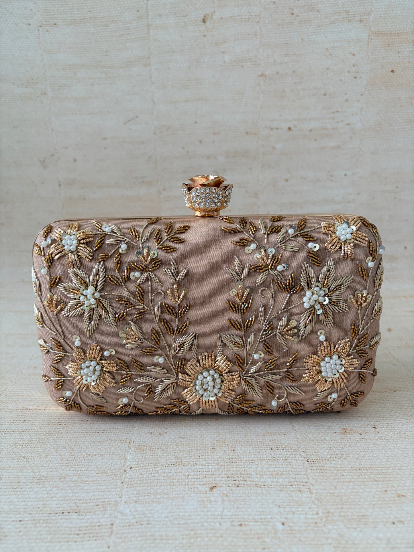 Decorative clutch bag with floral embroidery on a textured beige background