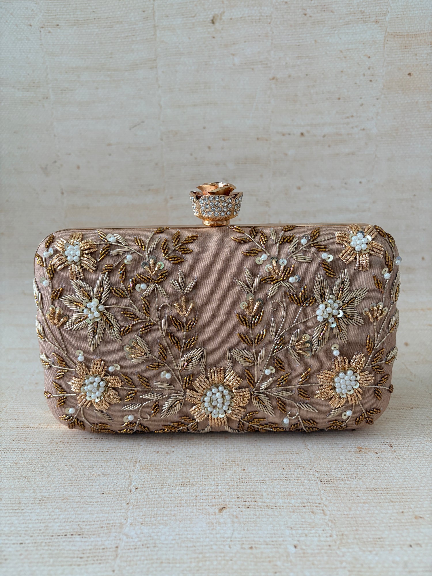 Decorative clutch bag with floral embroidery on a textured beige background