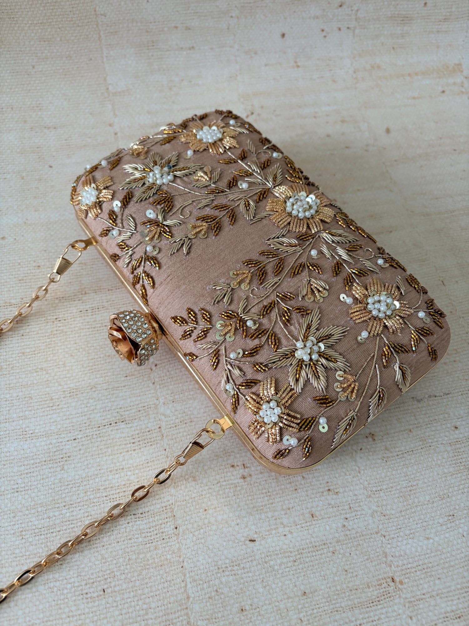 Decorative clutch bag with floral embroidery and a chain strap on a textured beige background