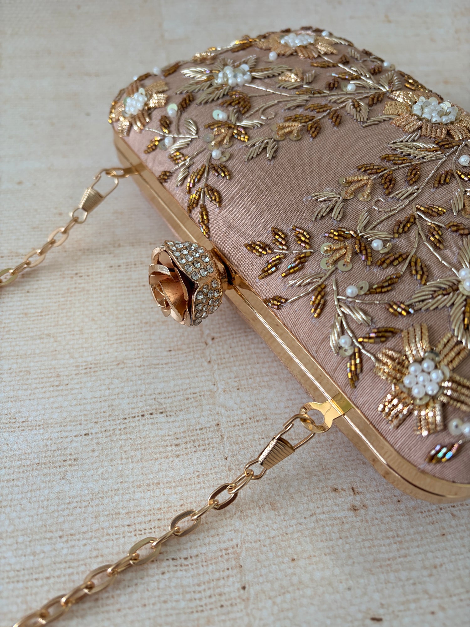 Pink handbag with gold embroidery and chain strap on a textured beige background