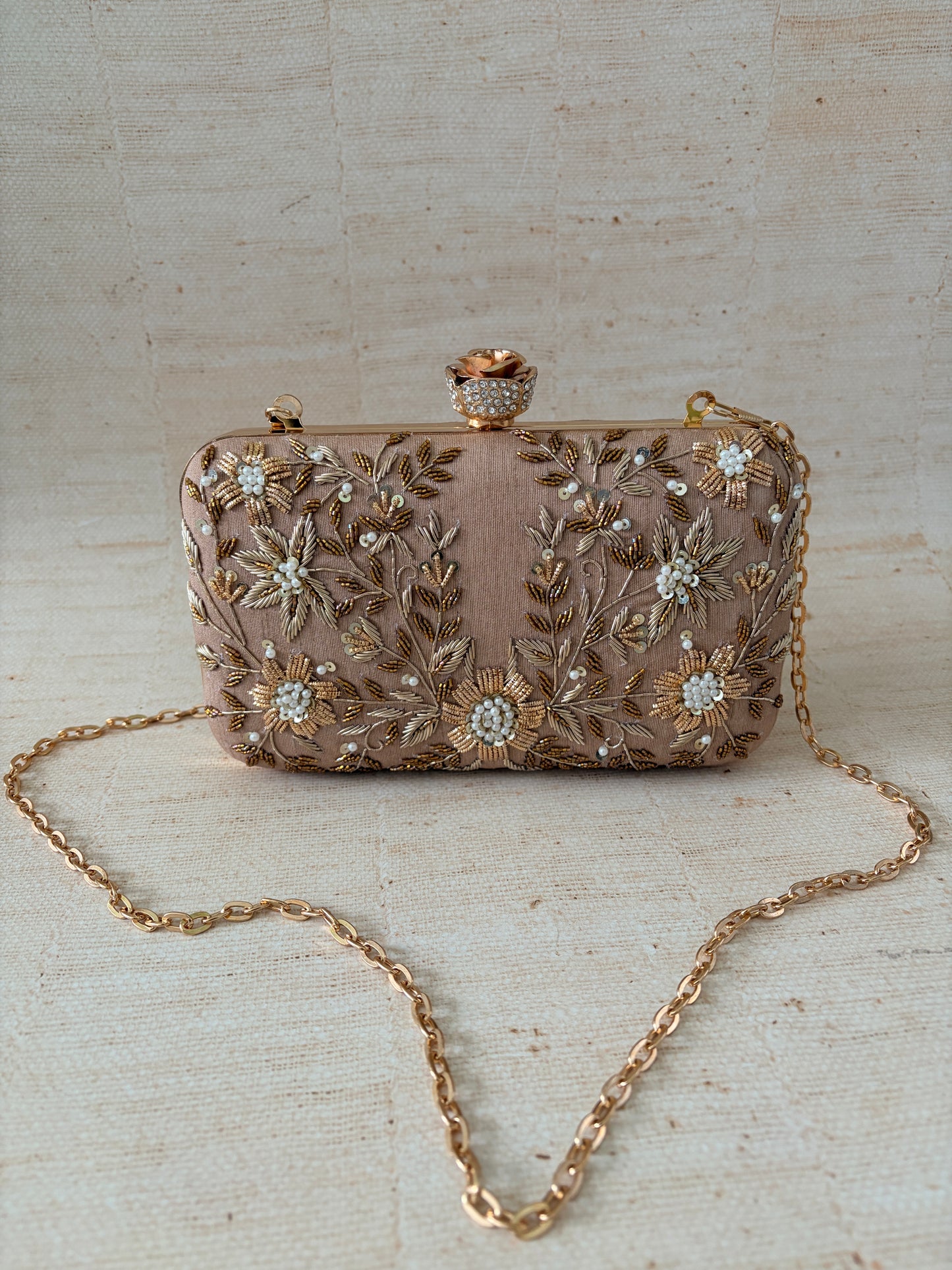 Decorative handbag with floral embroidery and a chain strap on a textured surface