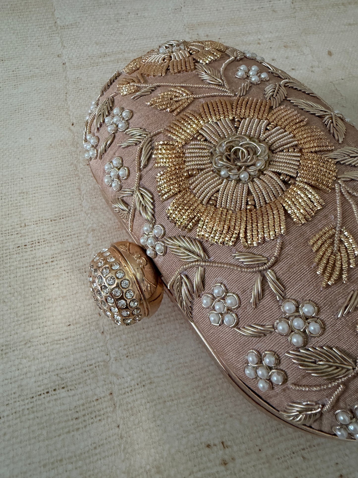 Decorative clutch with gold embroidery and pearl embellishments on a textured beige background